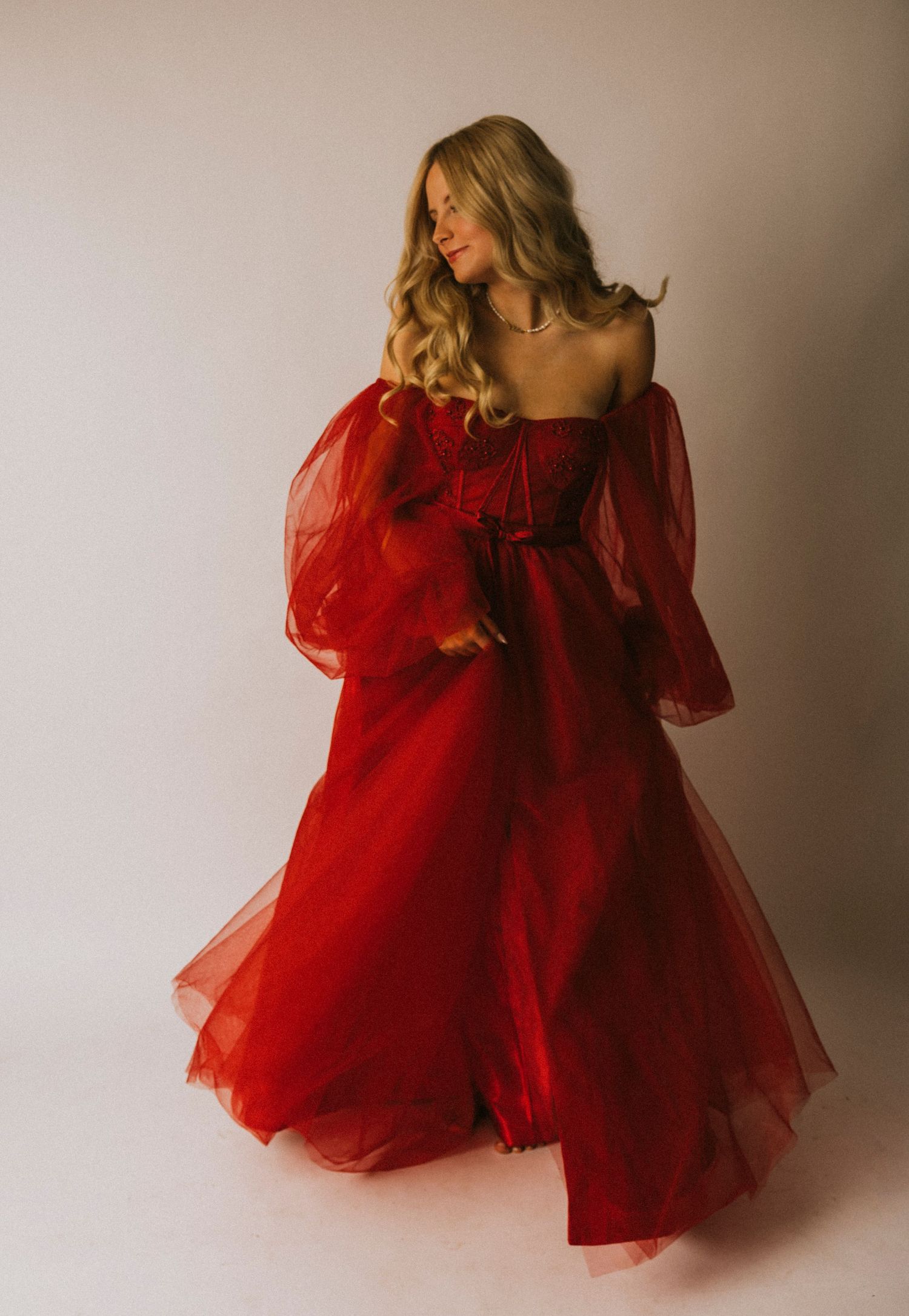 Abilene Senior High School girl in  flowing red tulle ball gown with puff sleeves, posing gracefully against a light gray background.