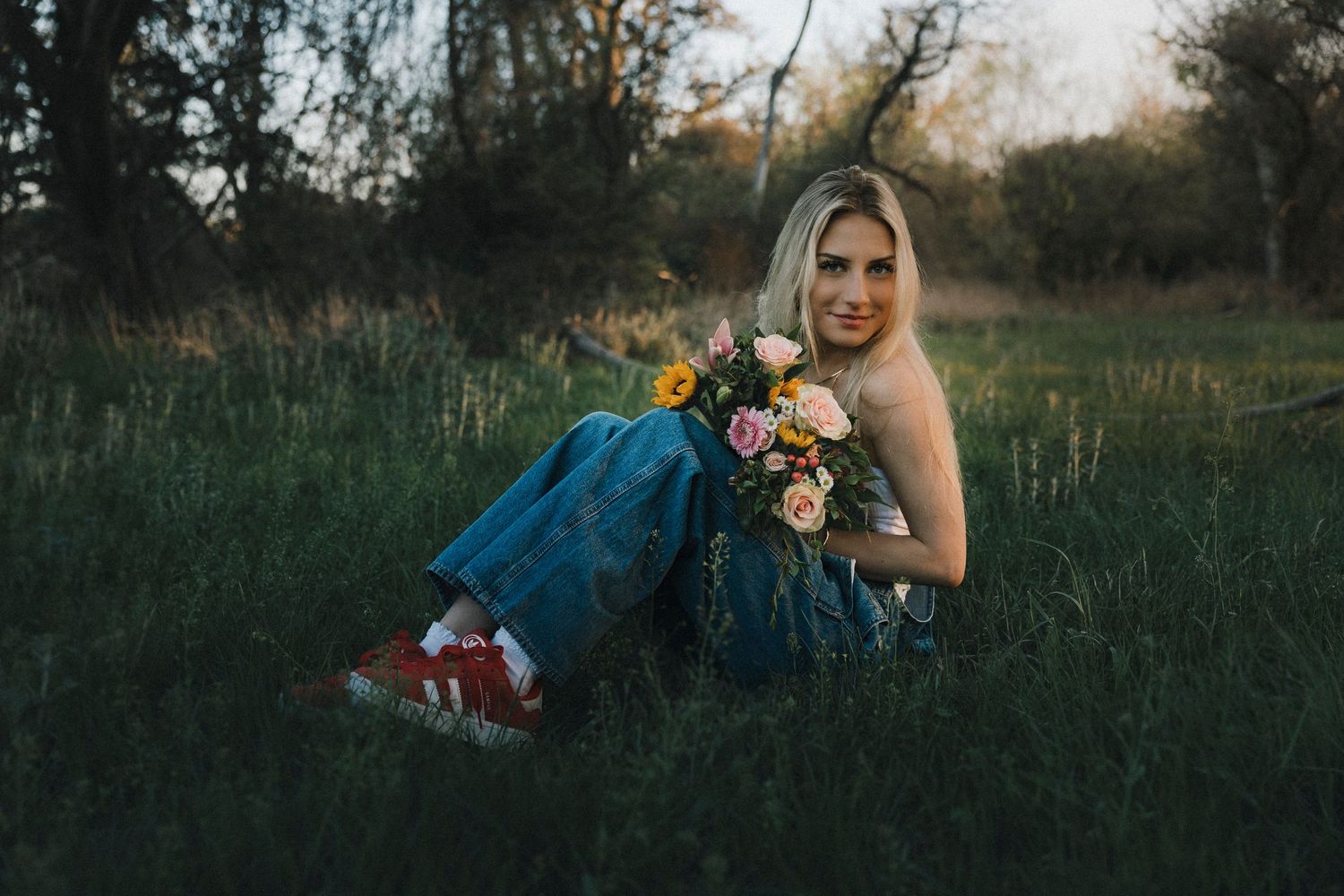 Blonde senior girl sitting in a grassy field holding flowers during golden hour senior portraits in Abilene TX