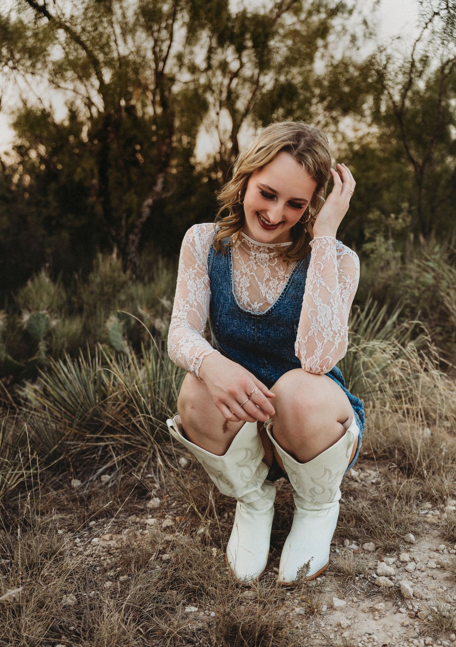 Smiling Class of 2027 senior crouching among native Texas grasses during a natural light senior portrait session in Abilene, Texas.