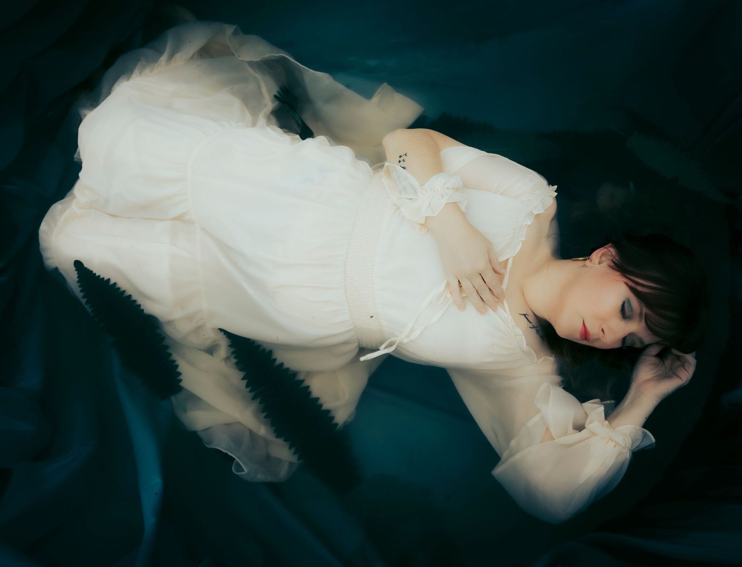 Moody portrait of a woman in a white gown floating on dark water with soft, ethereal movement