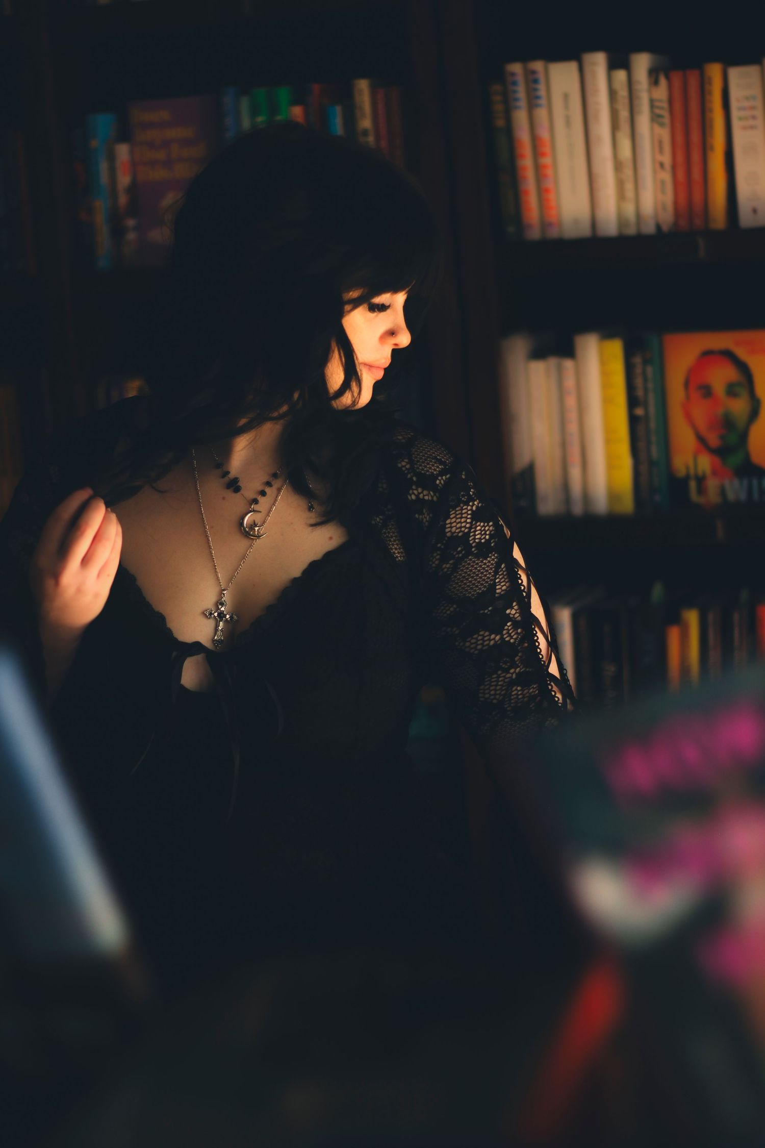Moody creative portrait session in Abilene TX featuring a subject standing among bookshelves with cinematic low light and shadow