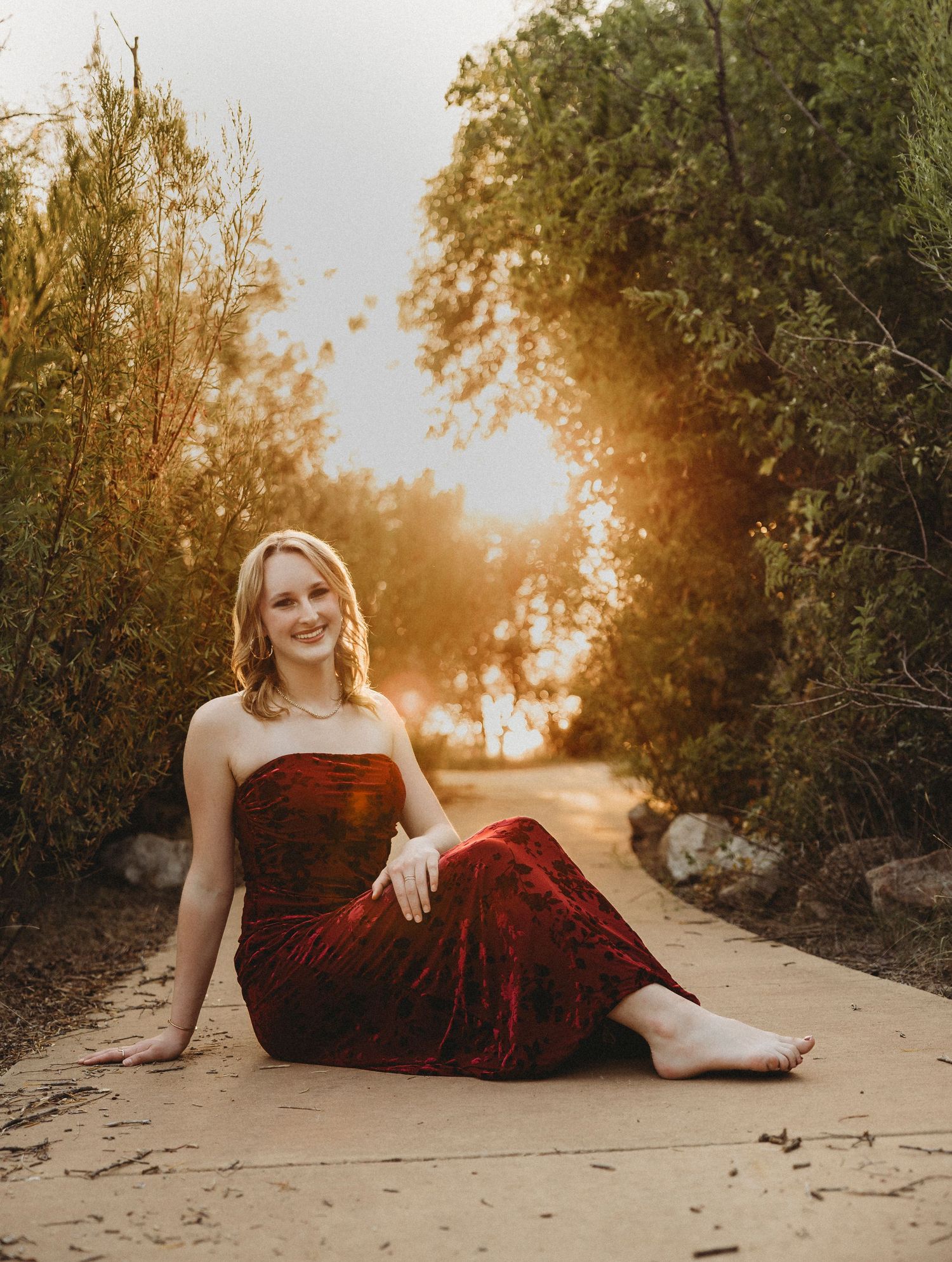 High school senior posing in a burgundy dress with warm golden hour light during an outdoor senior portrait session in Abilene, Texas.