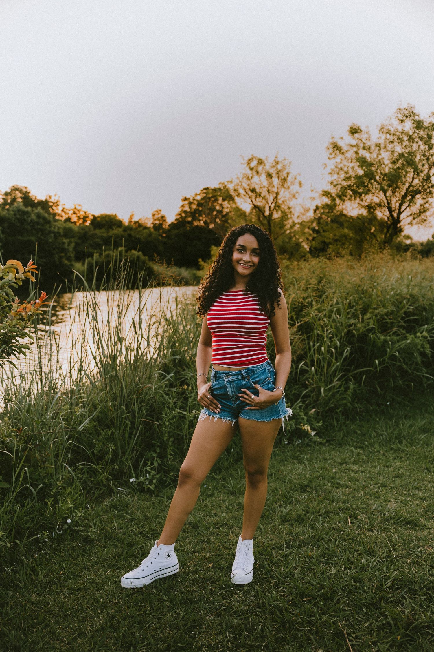Outdoor senior portrait of a Class of 2027 senior standing near a pond during a golden hour photography session in Abilene, Texas.
