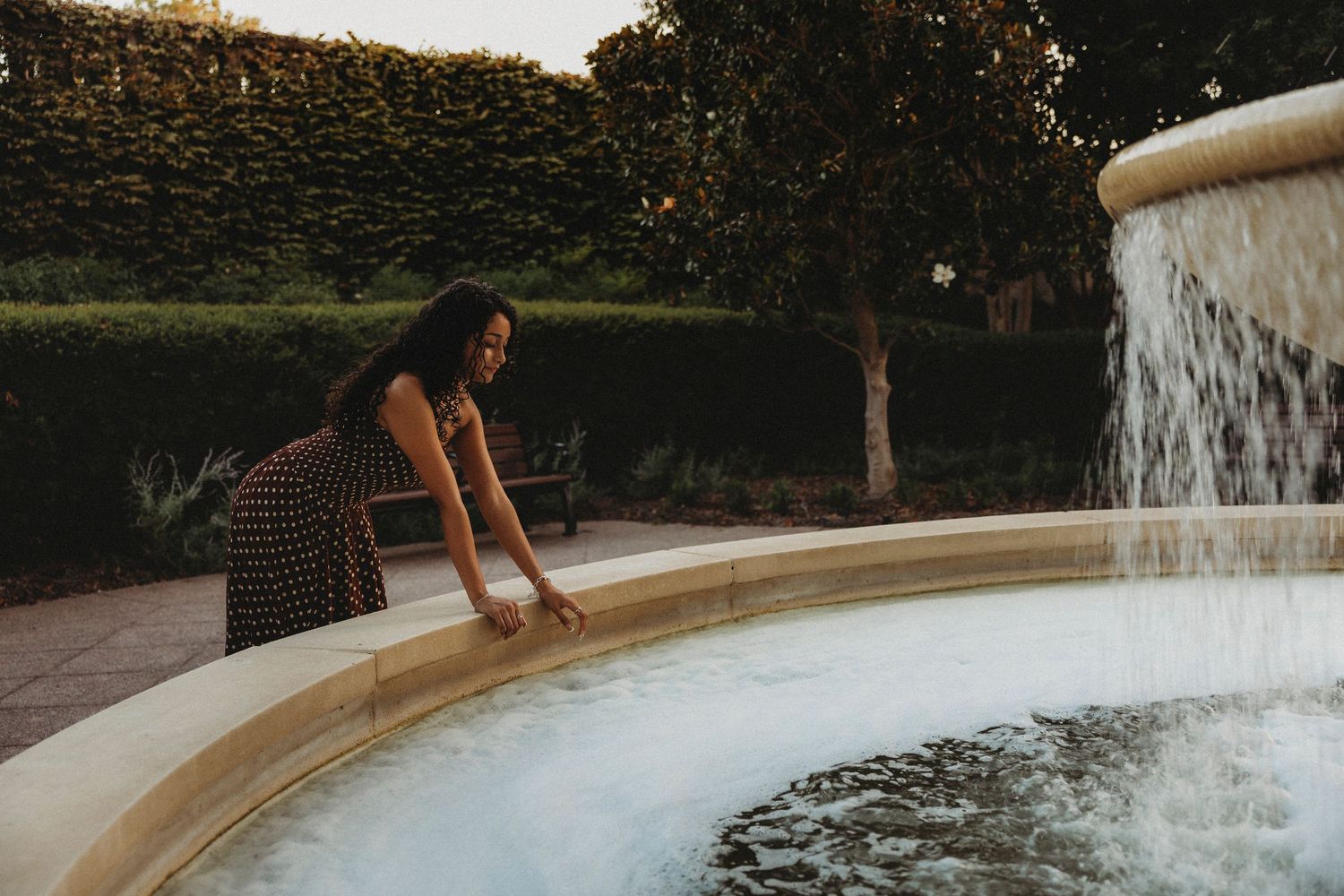 Class of 2027 Cooper High School senior leaning over a downtown Abilene fountain during an outdoor golden hour senior photography session.