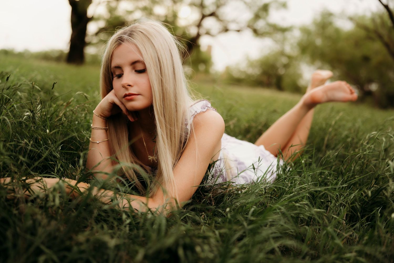 Blonde high school senior laying in tall grass during outdoor senior photo session in Abilene TX