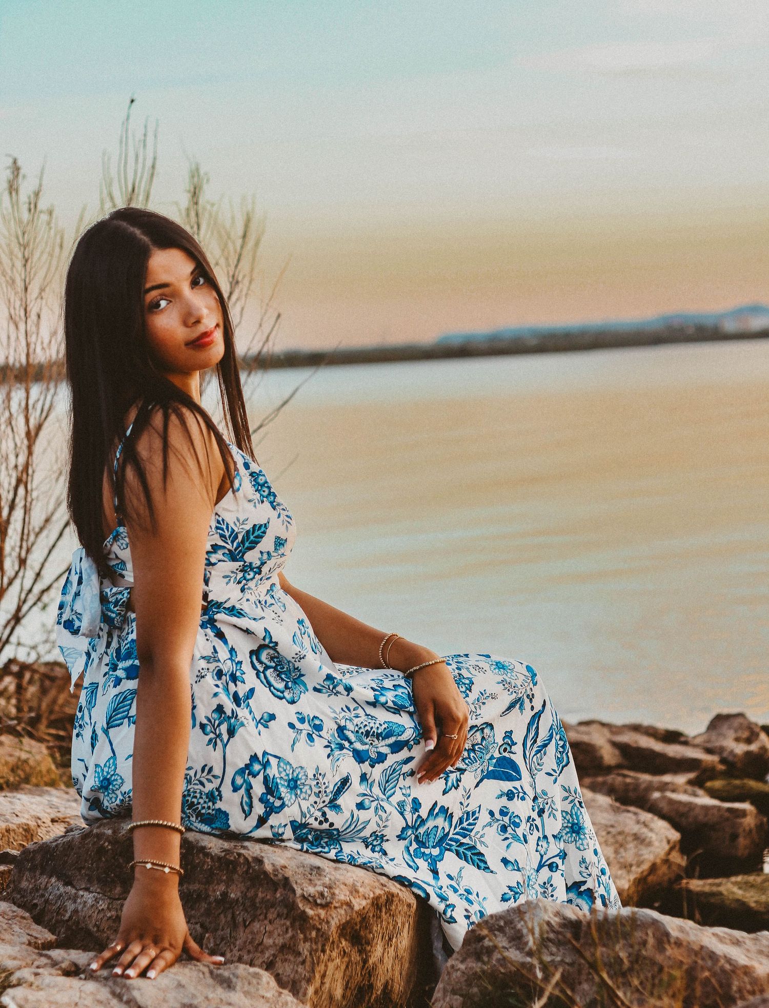 Outdoor senior portrait session in Abilene TX featuring a high school senior sitting on rocks by the water during golden hour