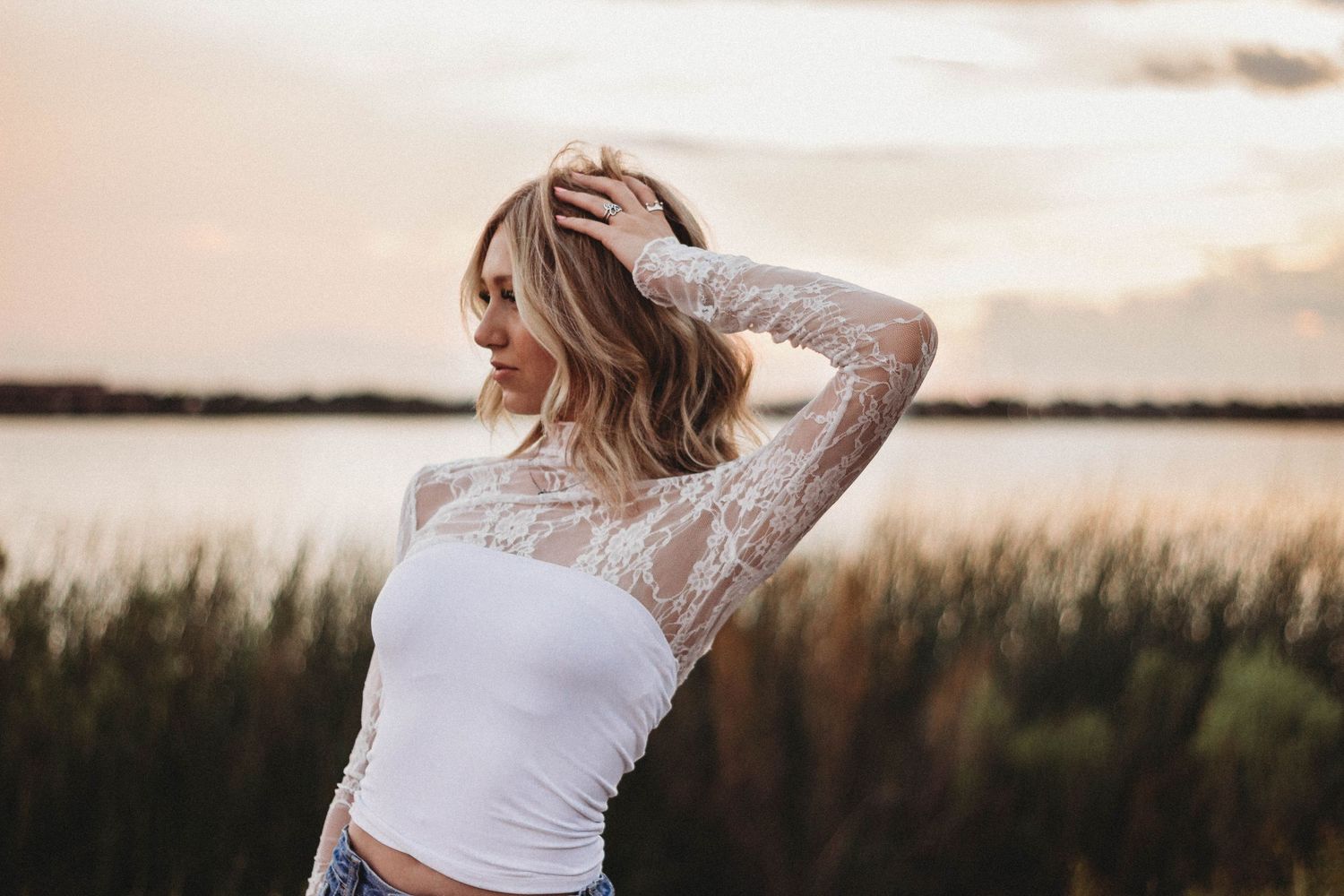 A person in a white top poses in a natural outdoor setting during golden hour lighting.