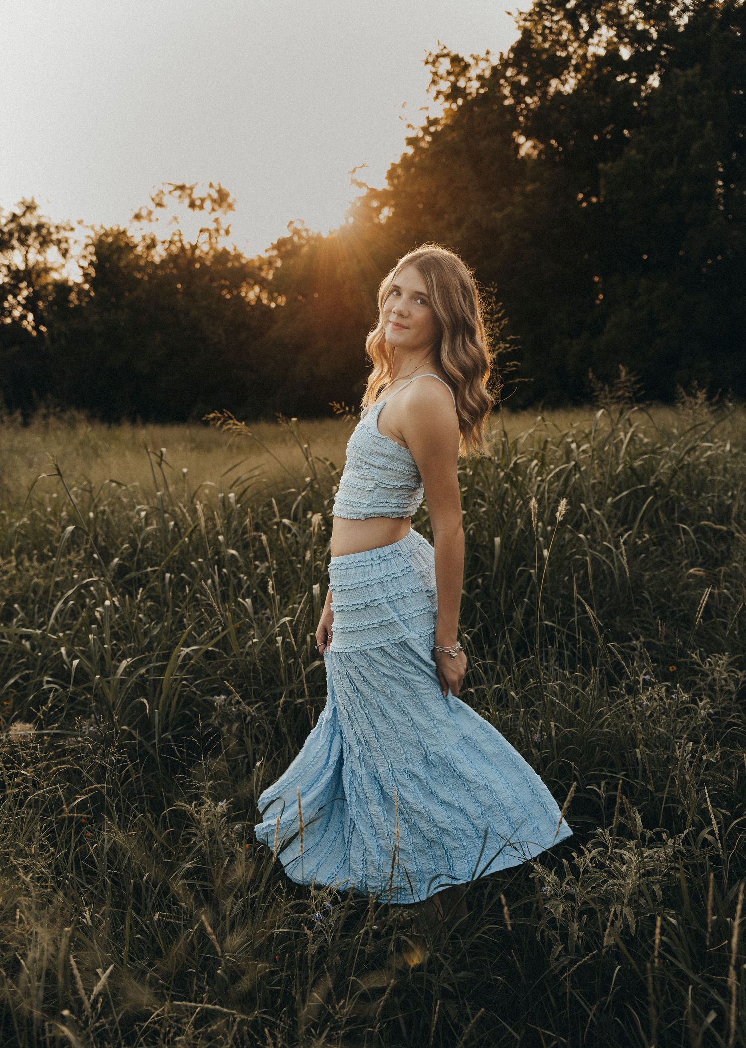 High school senior twirling in a flowing blue dress in a sunlit field during a golden hour senior photography session in Abilene, Texas.