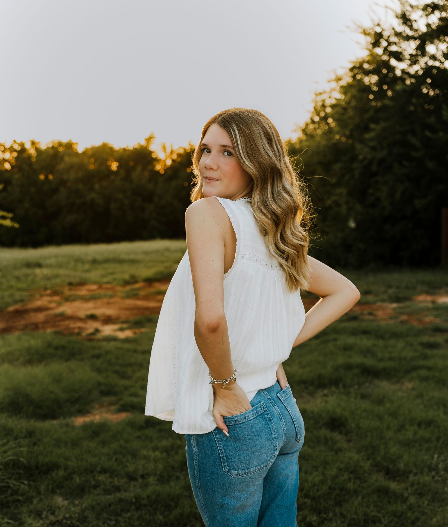 High school senior wearing a white sleeveless top and blue jeans looking over her shoulder during an outdoor senior portrait session in Abil
