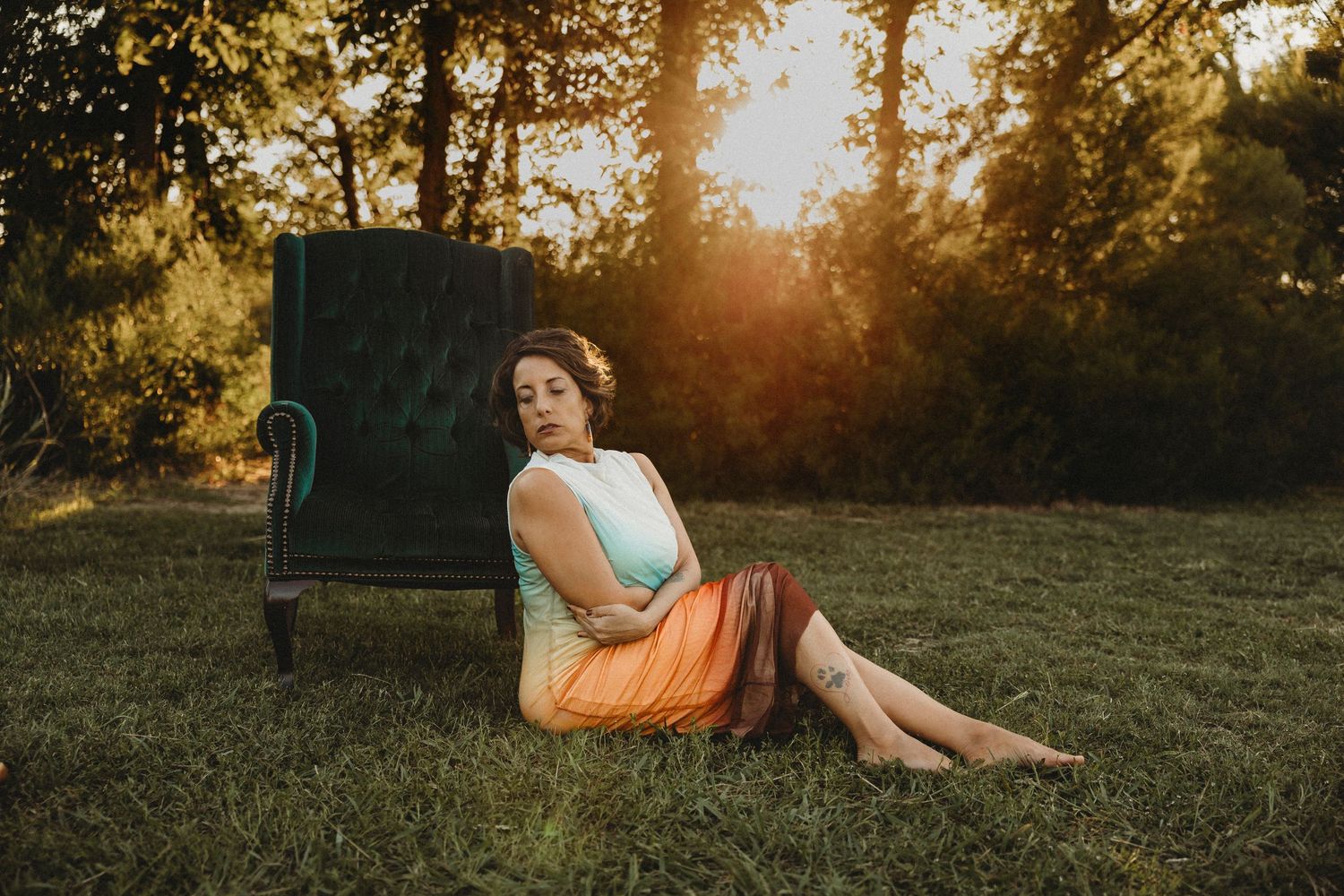 Woman sitting beside a vintage green velvet chair during a golden hour outdoor portrait session in Abilene, Texas.