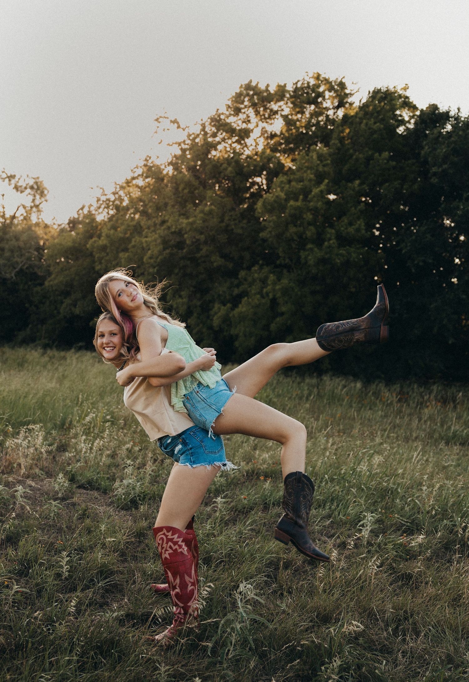 Two best friends laugh and play in a grassy field during a golden hour friendship photoshoot in Abilene, Texas. Fun outdoor senior and best