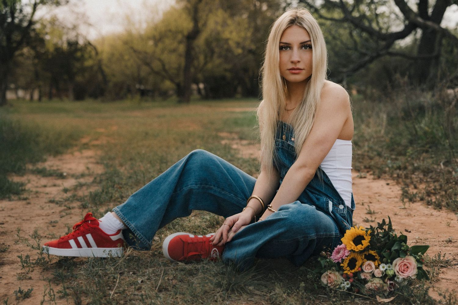 High school senior sitting on a dirt path with sunflowers during a personalized senior photo session in Abilene, Texas