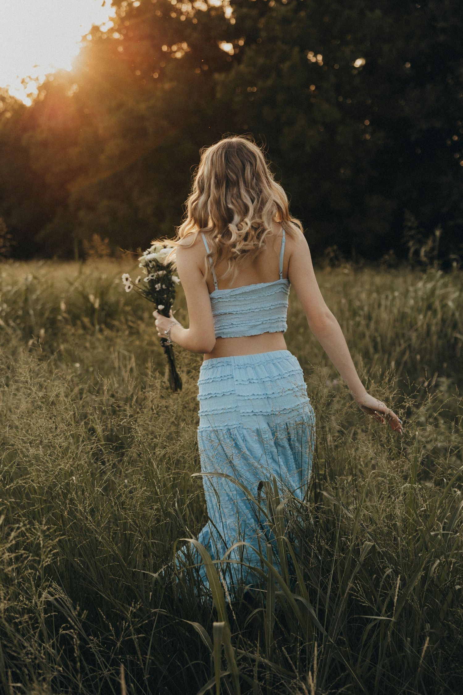 high school senior walking through a wildflower field at sunset during an outdoor senior portrait session in Abilene, Texas.