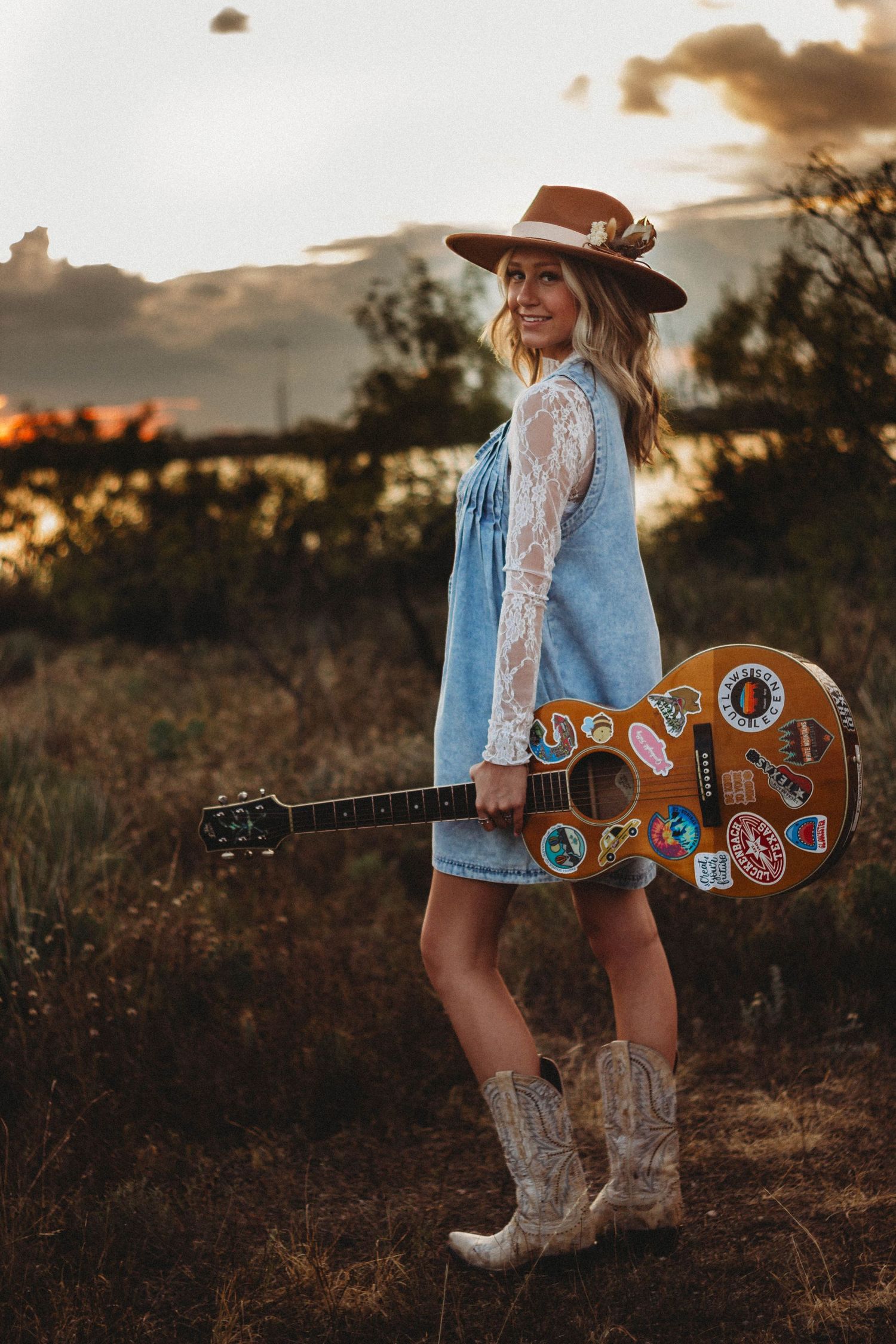 High school senior wearing a cowboy hat and boots while holding a colorful guitar during a western-inspired senior photo session in Abilene,