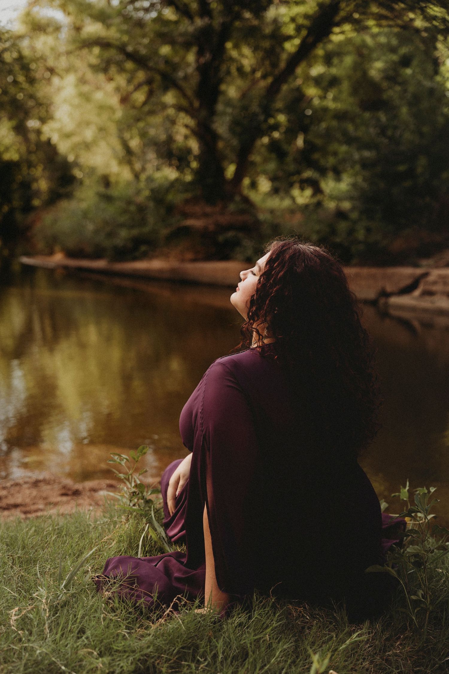 Outdoor senior portrait of a Jim Ned High School senior in a flowing plum dress sitting beside a creek during