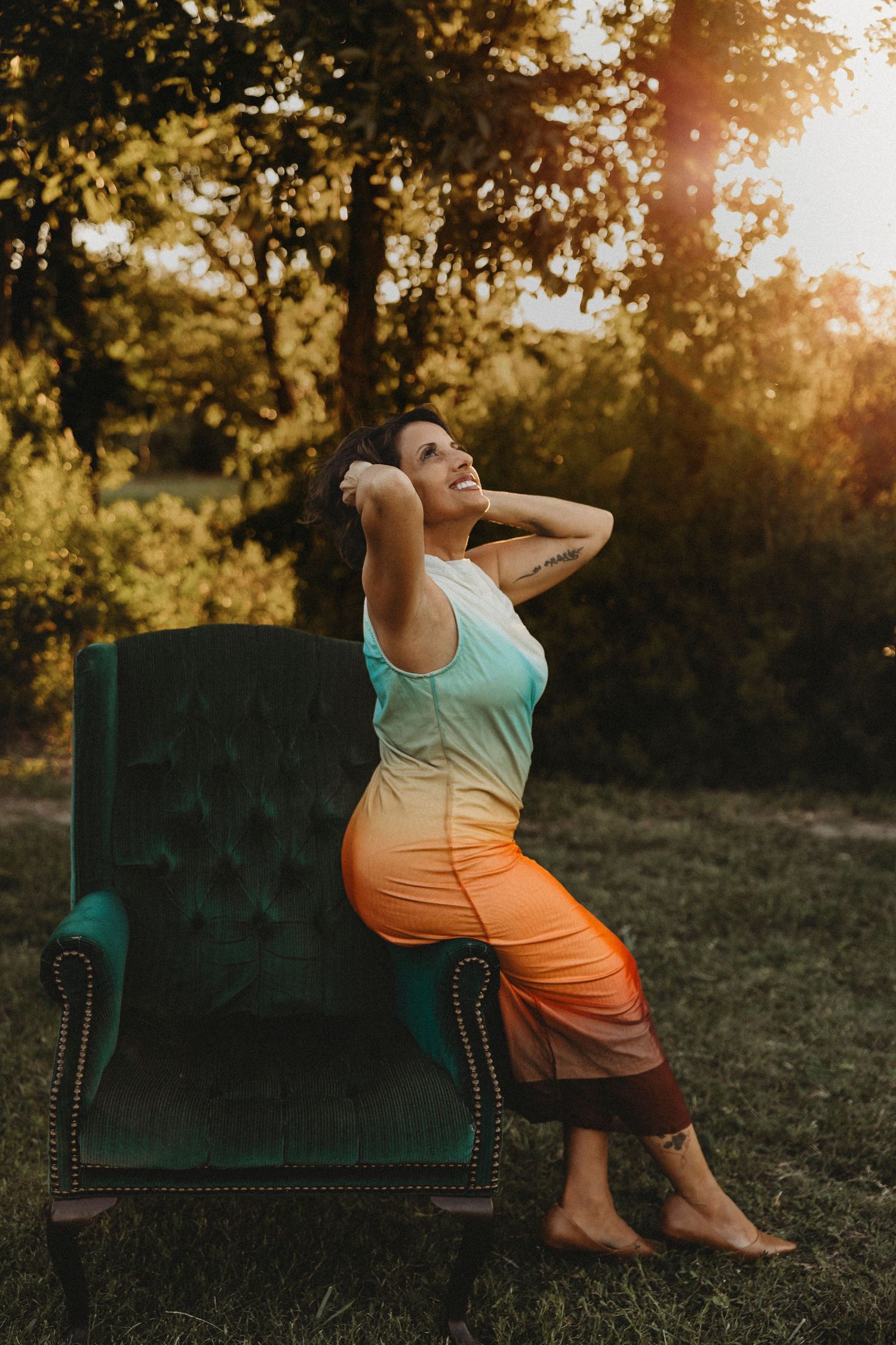 Portrait of a woman posing in a vintage green wingback chair during a golden hour outdoor photography session in Abilene, Texas.