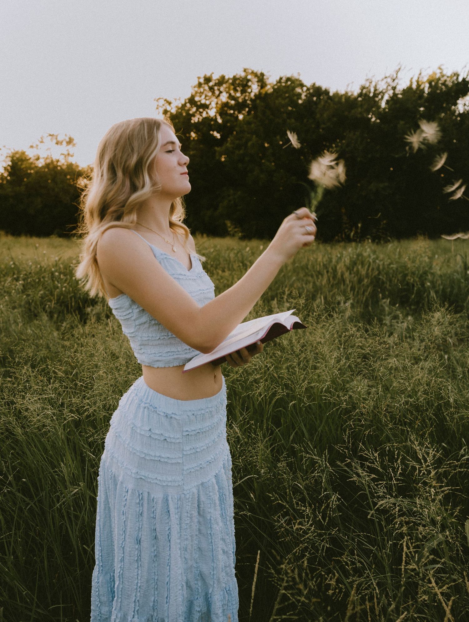 High school senior in a light blue dress holding a dandelion during a golden hour senior portrait session in Abilene, Texas.