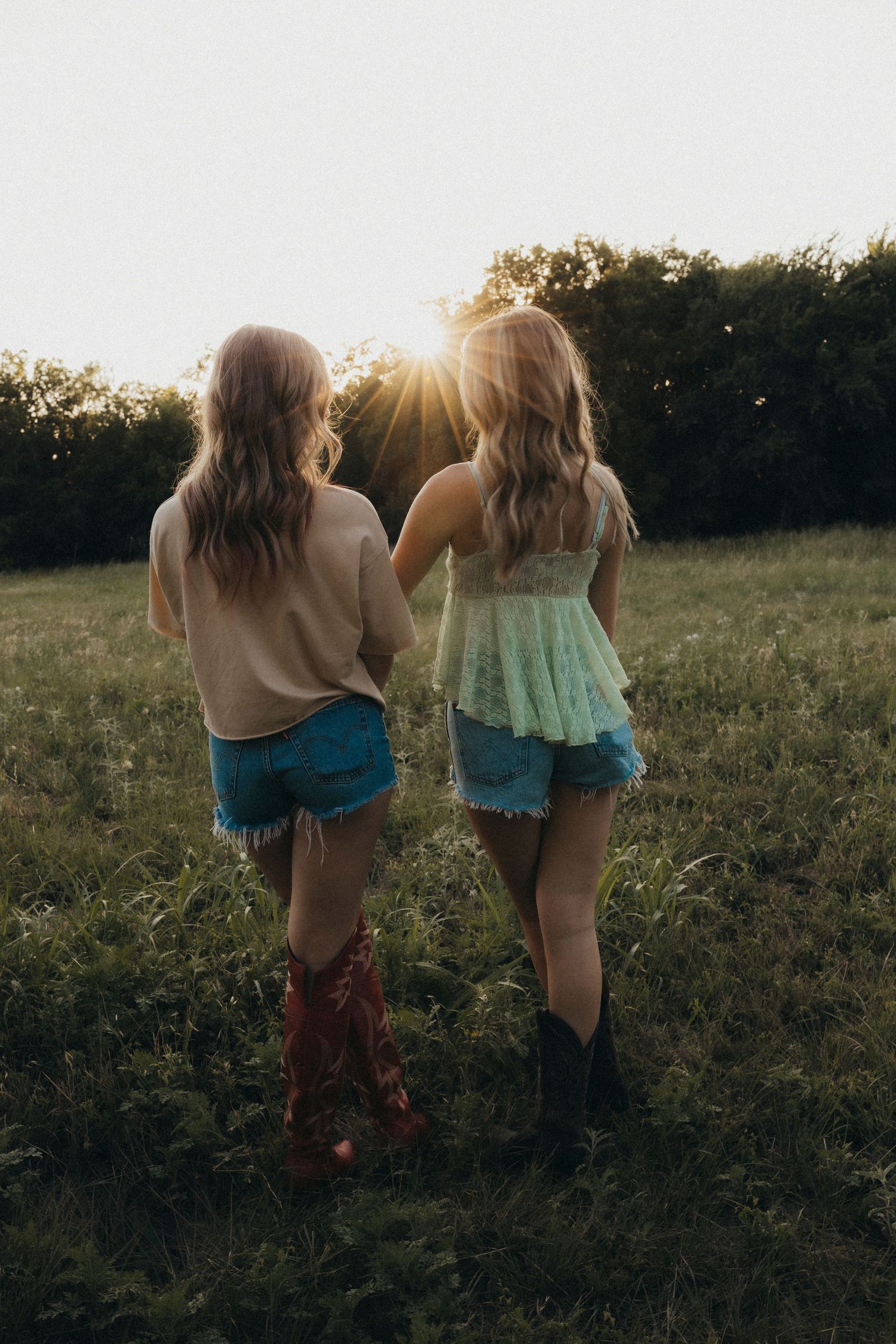 Two best friends walk through a sunlit field at sunset during a candid outdoor friendship session in Abilene, Texas.