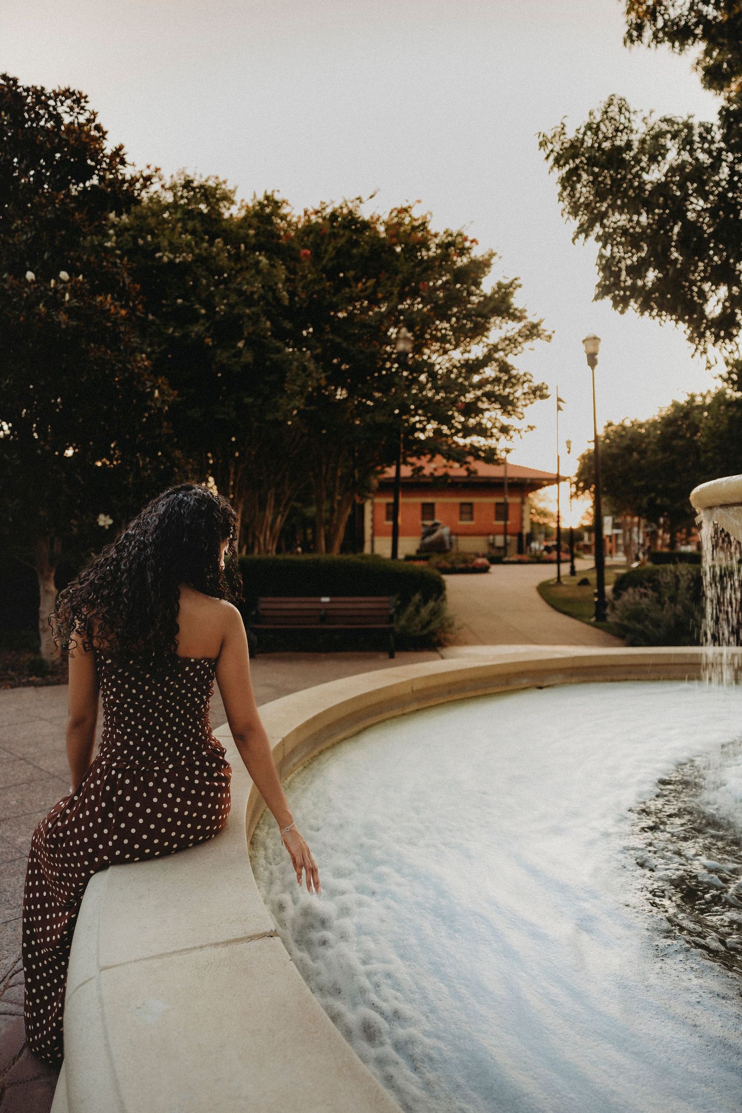 Class of 2027 Cooper High School senior leaning over a downtown Abilene fountain during an outdoor golden hour senior photography session.
