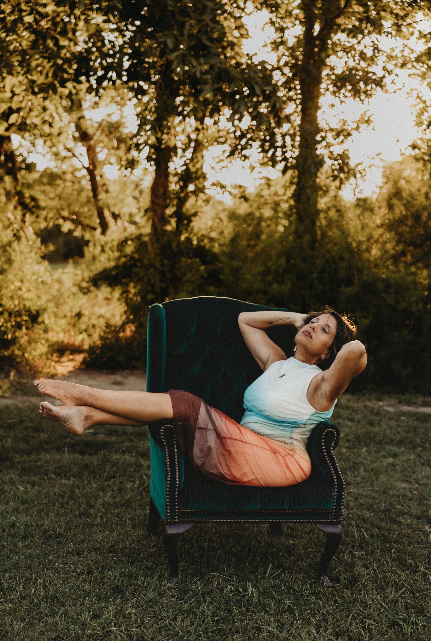 Woman reclining in a vintage green velvet chair during a creative outdoor portrait session at sunset in Abilene, Texas.