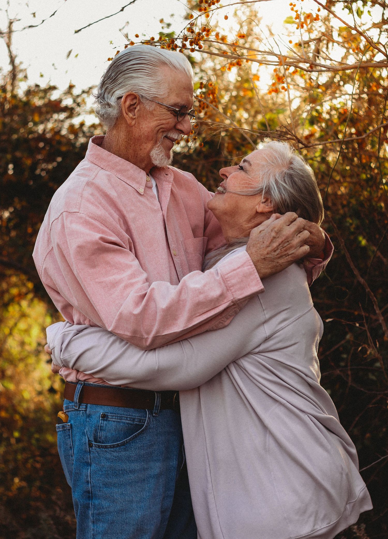 Happy elderly couple embracing and smiling outdoors in autumn, sharing a romantic moment surrounded by fall foliage.