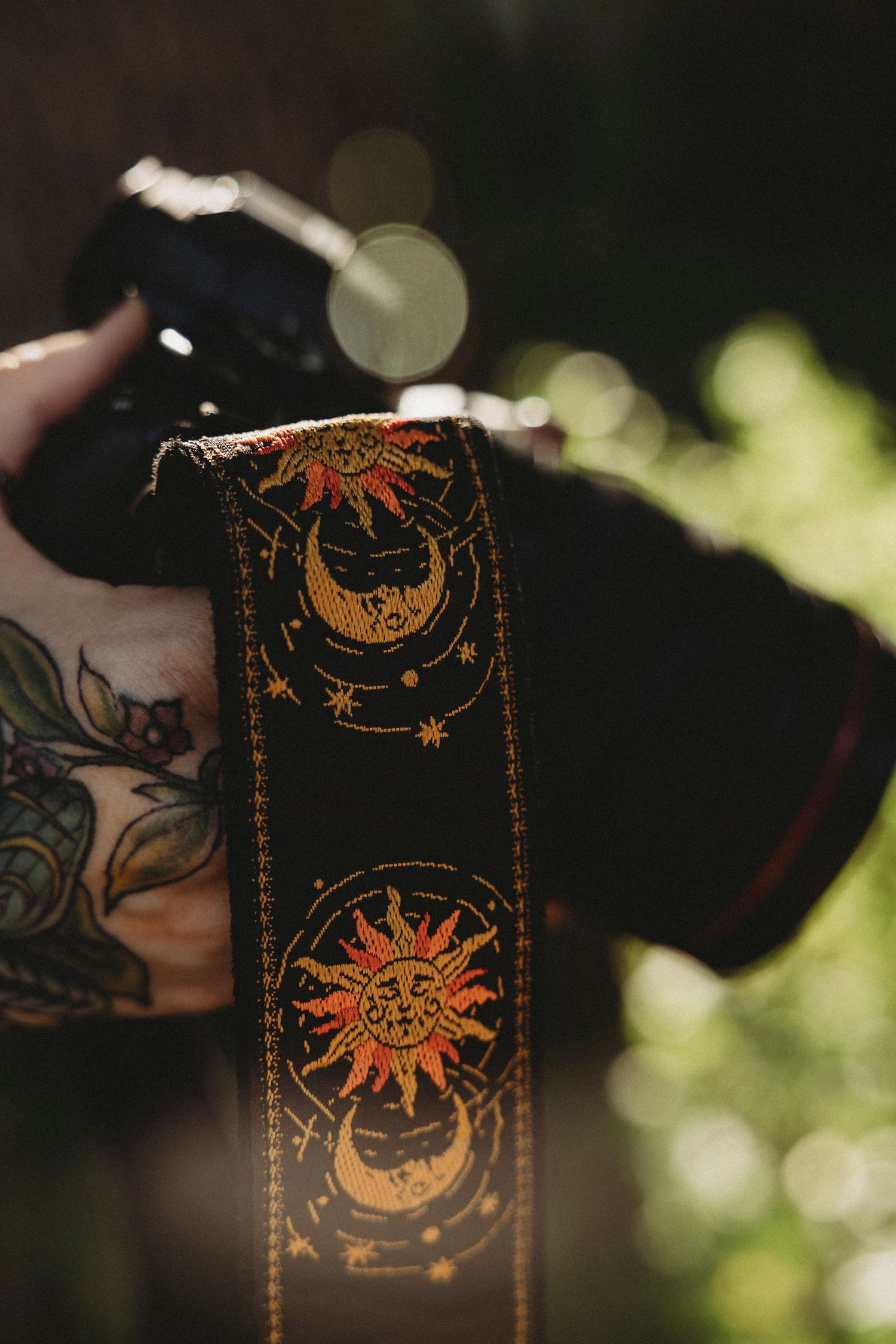 Close-up of photographer holding camera with detailed camera strap in warm natural light.