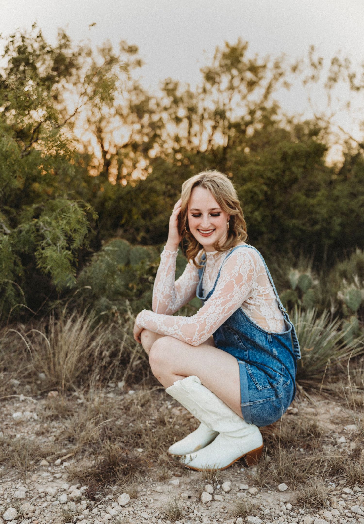 High school senior crouching among native Texas grasses during a golden hour senior portrait session in Abilene, Texas.