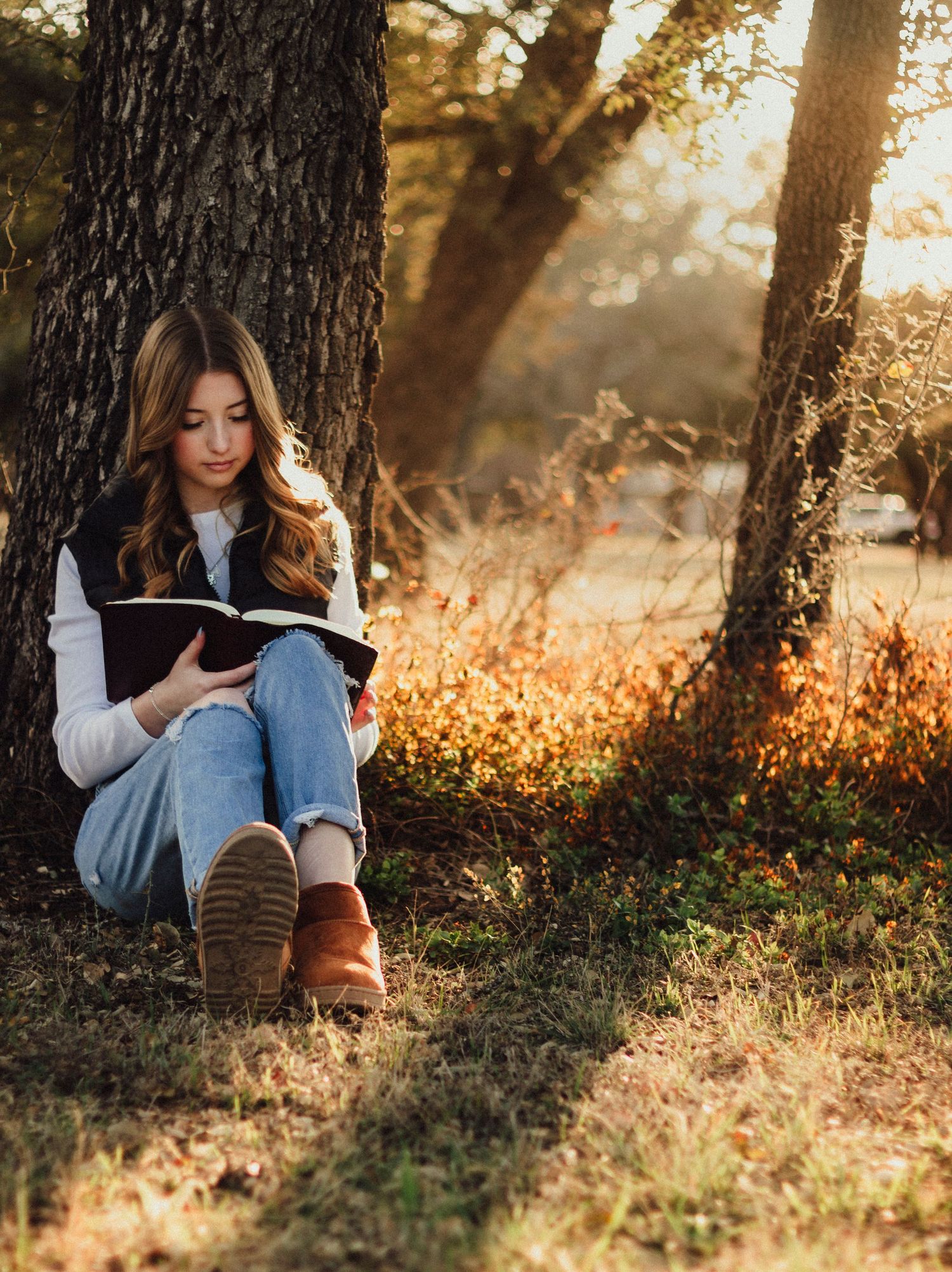 Abilene TX senior photographer capturing Texas senior photos of a high school senior sitting under a tree at sunset reading her Bible