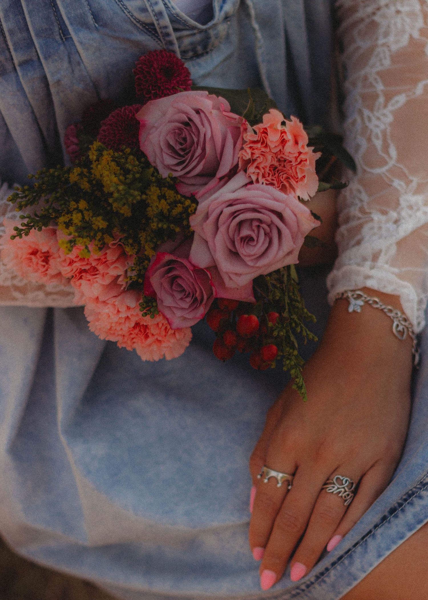 Close-up view of pink and coral roses with delicate greenery adorning a lace-detailed dress sleeve.