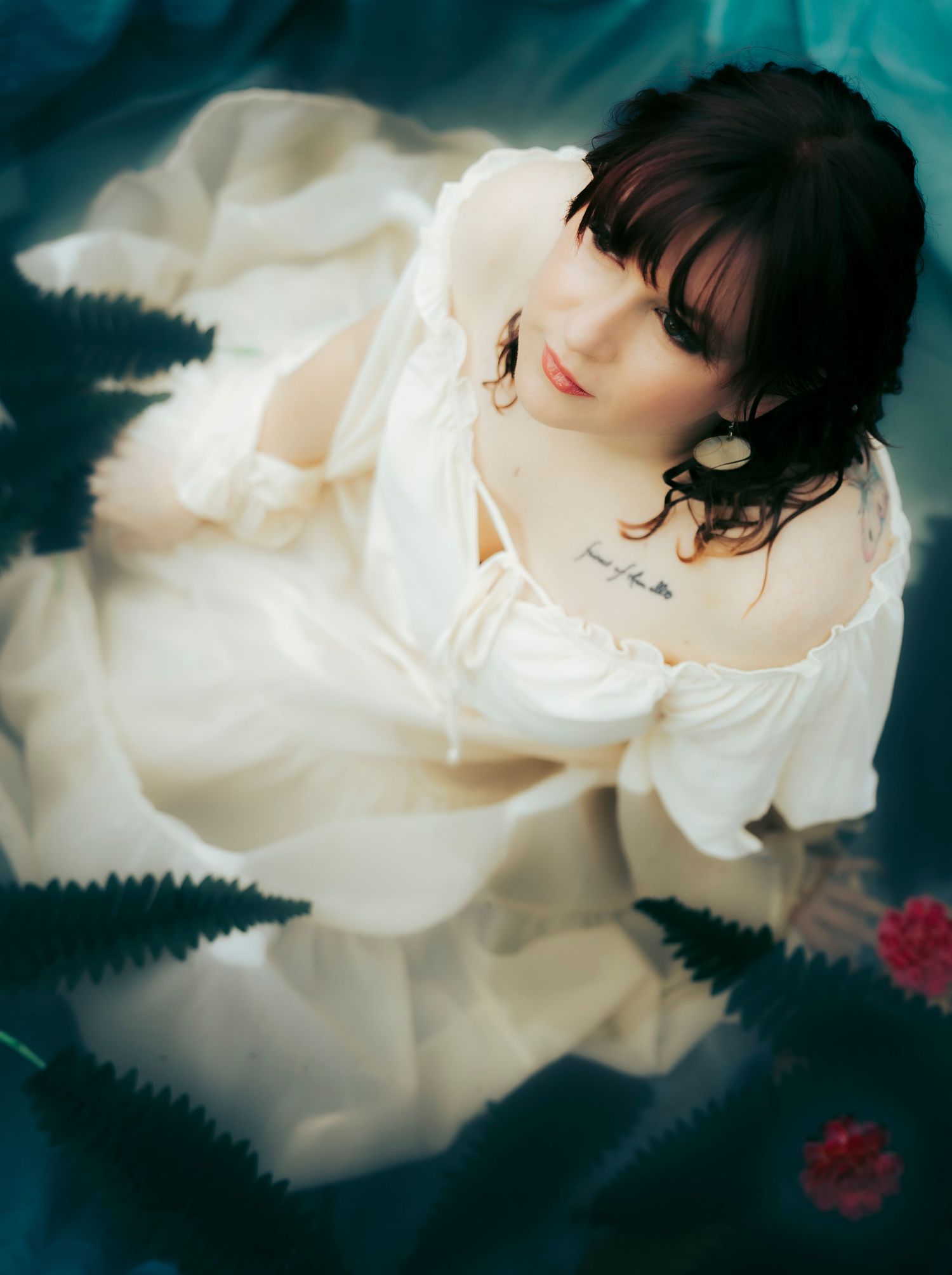 Moody portrait of a woman in a white gown sitting on dark water with soft, ethereal movement