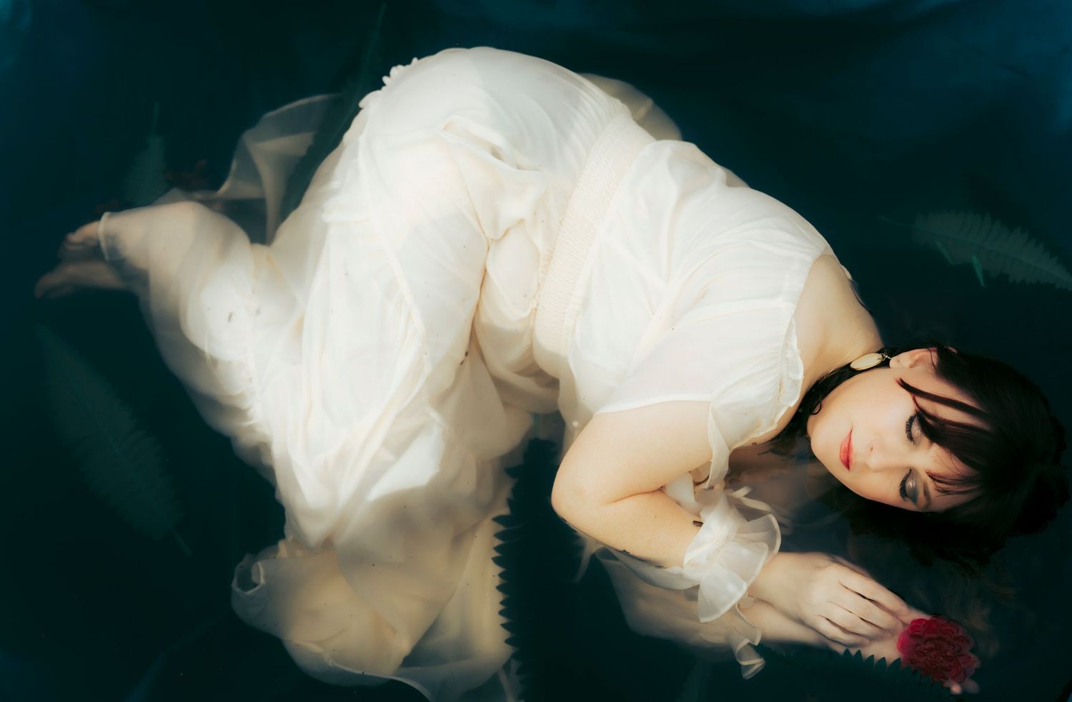 Woman in a flowing white dress floating in still water during a fine art portrait session in Abilene, Texas