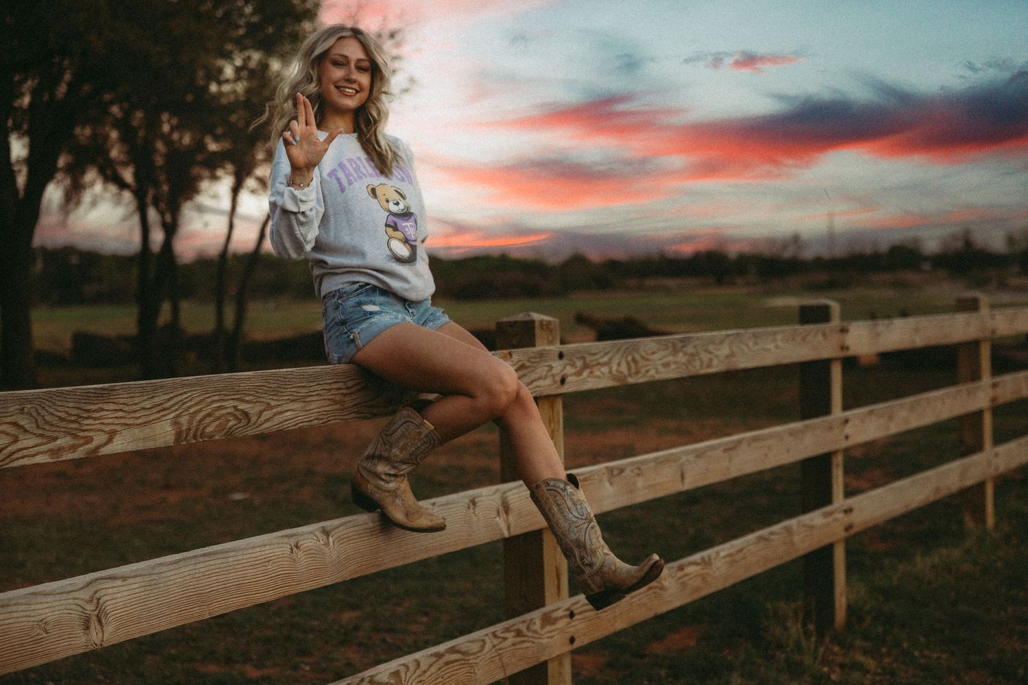 High school senior sitting on a wooden fence at sunset during an outdoor senior photoshoot in Abilene, Texas