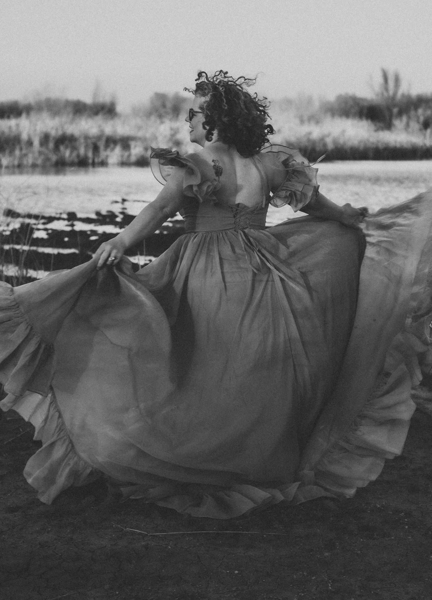 Styled portrait session in Abilene, Texas featuring a model twirling in a flowing teal gown at sunset near the water