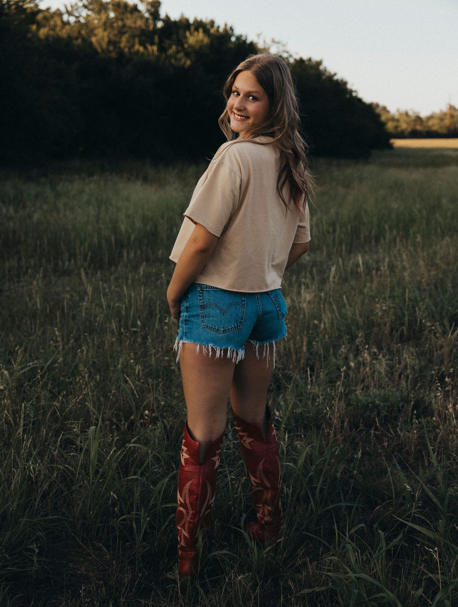 Outdoor senior photos of a Class of 2027 senior in western boots walking through a field during a golden hour senior portrait session