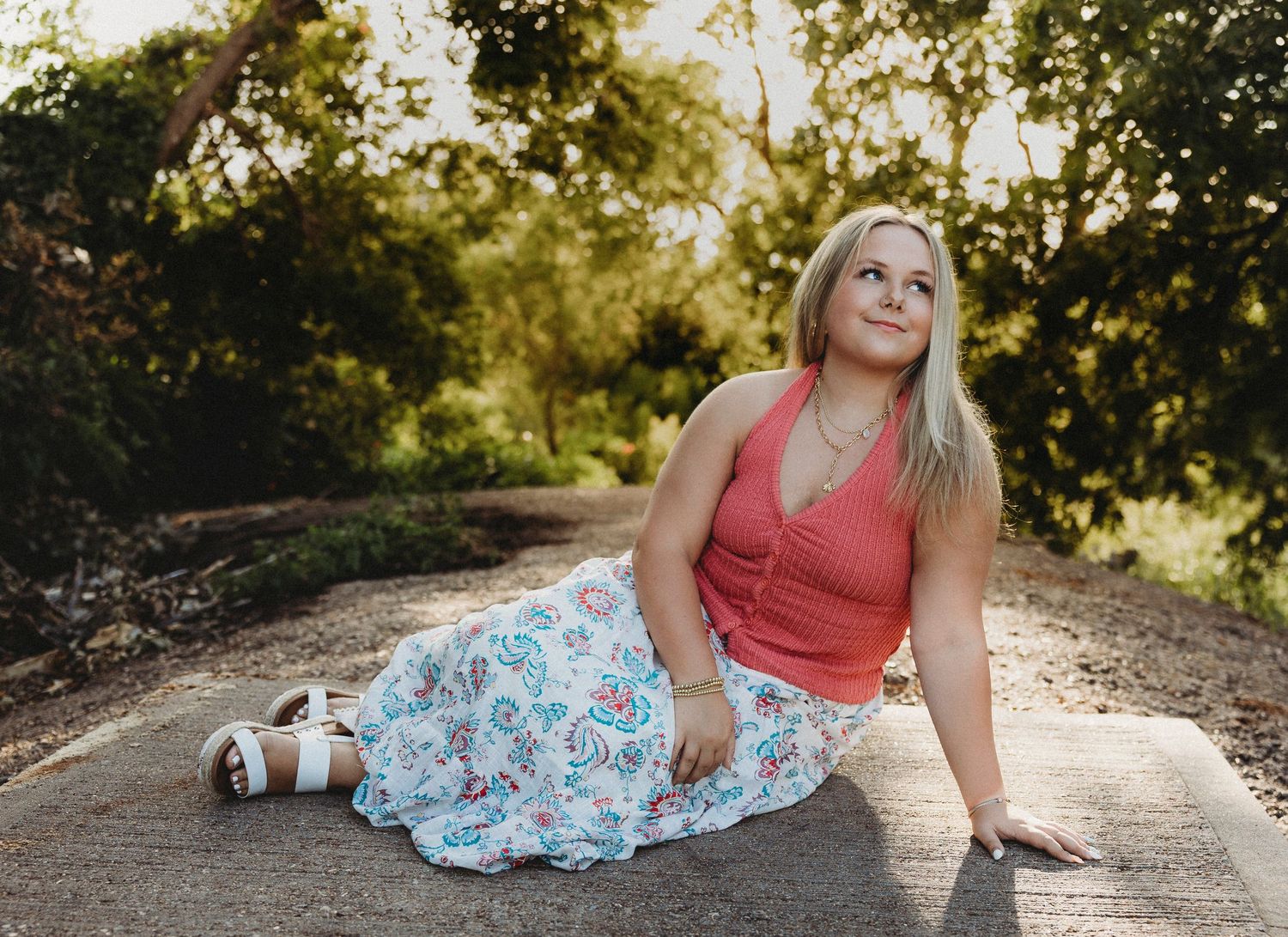 Wylie High School senior sitting on a quiet road during golden hour in a floral skirt and pink top for senior portraits in Abilene, Texas.