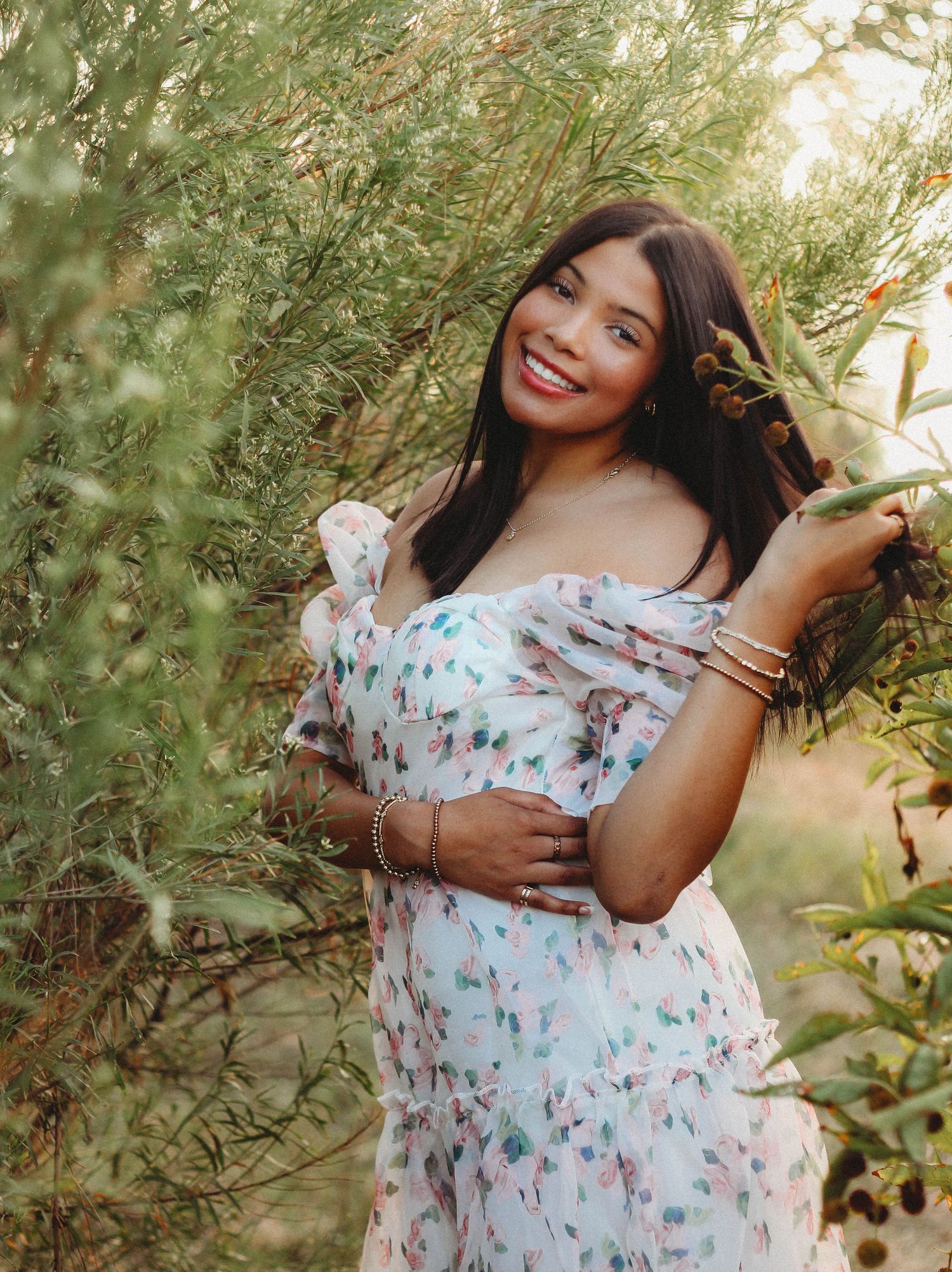 A woman in a floral off-shoulder dress poses outdoors among green foliage in a series of natural light portraits.