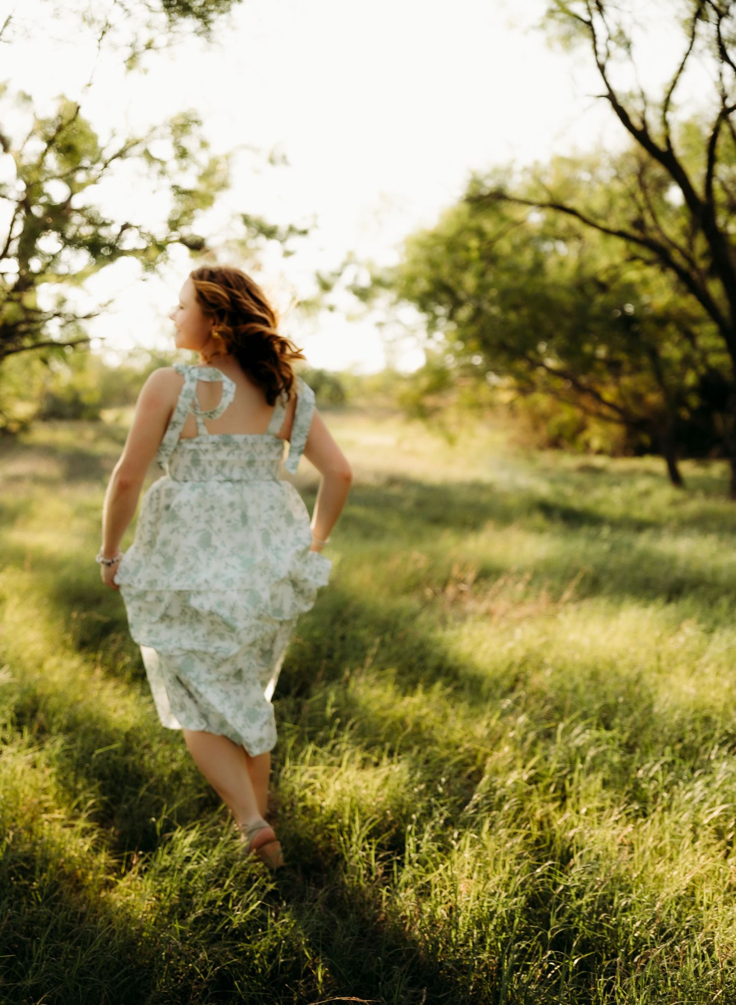 Senior girl walking through a sunlit field during golden hour senior portraits in Abilene Texas