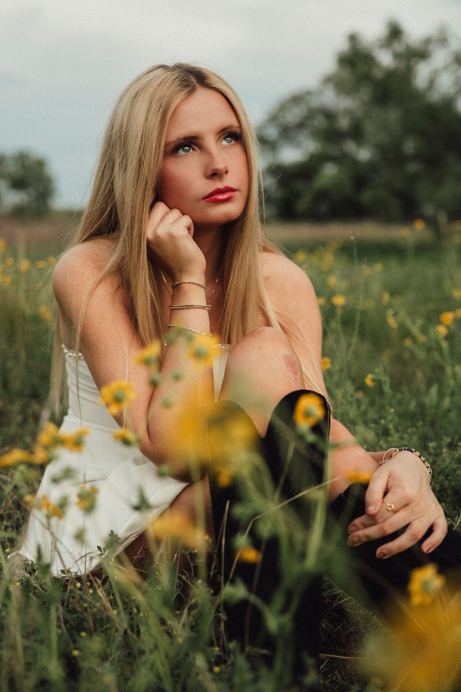 High School Senior in white dress sitting in a field of yellow wildflowers, gazing upward thoughtfully. In Abilene,TX
