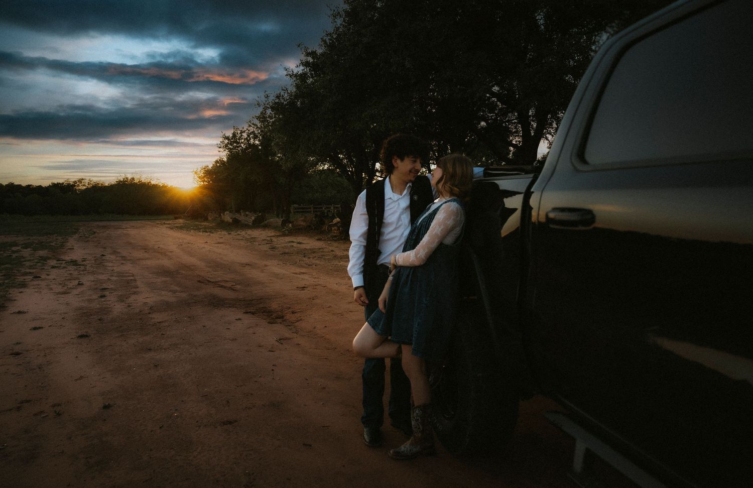 Couple sharing a romantic moment leaning against a truck at sunset on a dirt road.