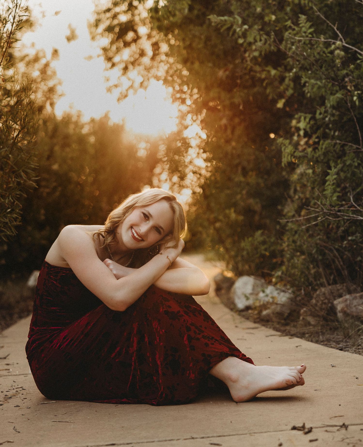 High school senior in a burgundy dress sitting beneath glowing sunset light during a cinematic outdoor senior portrait session in Abilene, T