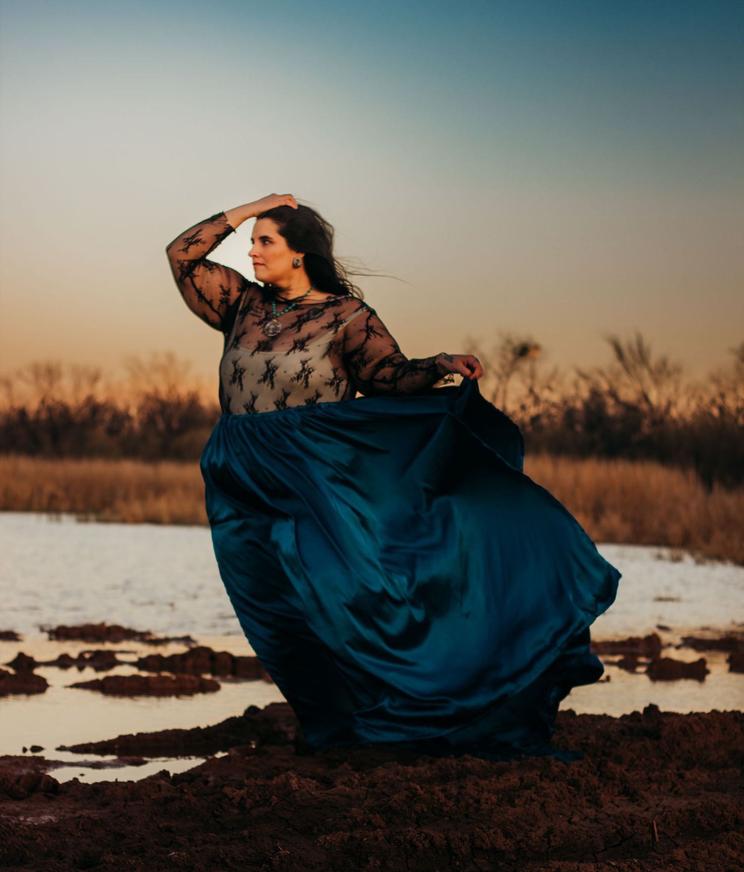 Fine art styled portrait session in Abilene Texas featuring a model in a flowing teal gown photographed at golden hour near the water