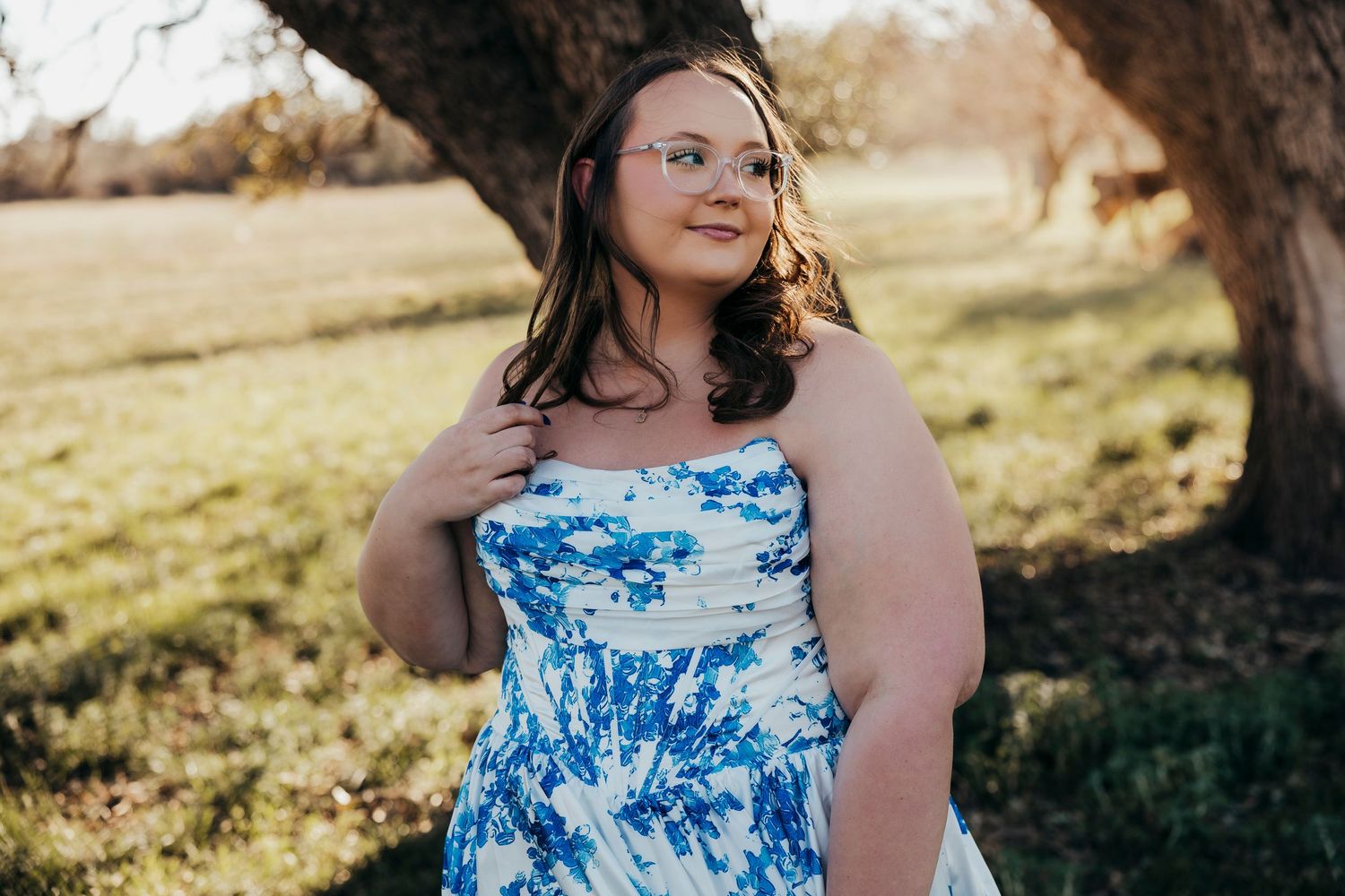High school senior girl in a blue floral dress standing in soft sunlight during an outdoor senior session in Abilene, TX.