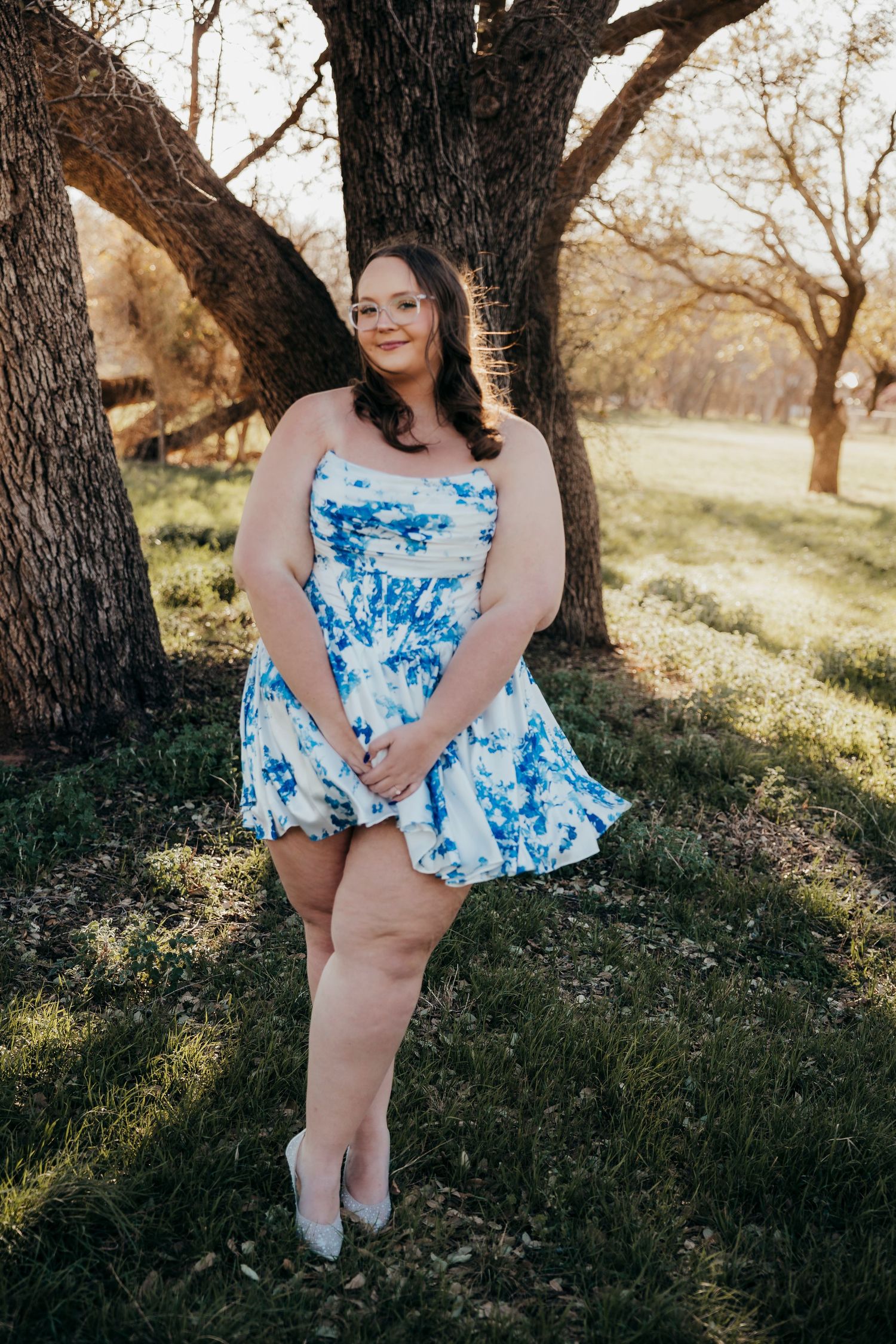 Senior girl  in a blue and white floral dress poses playfully in a field during golden hour in Buffalo Gap