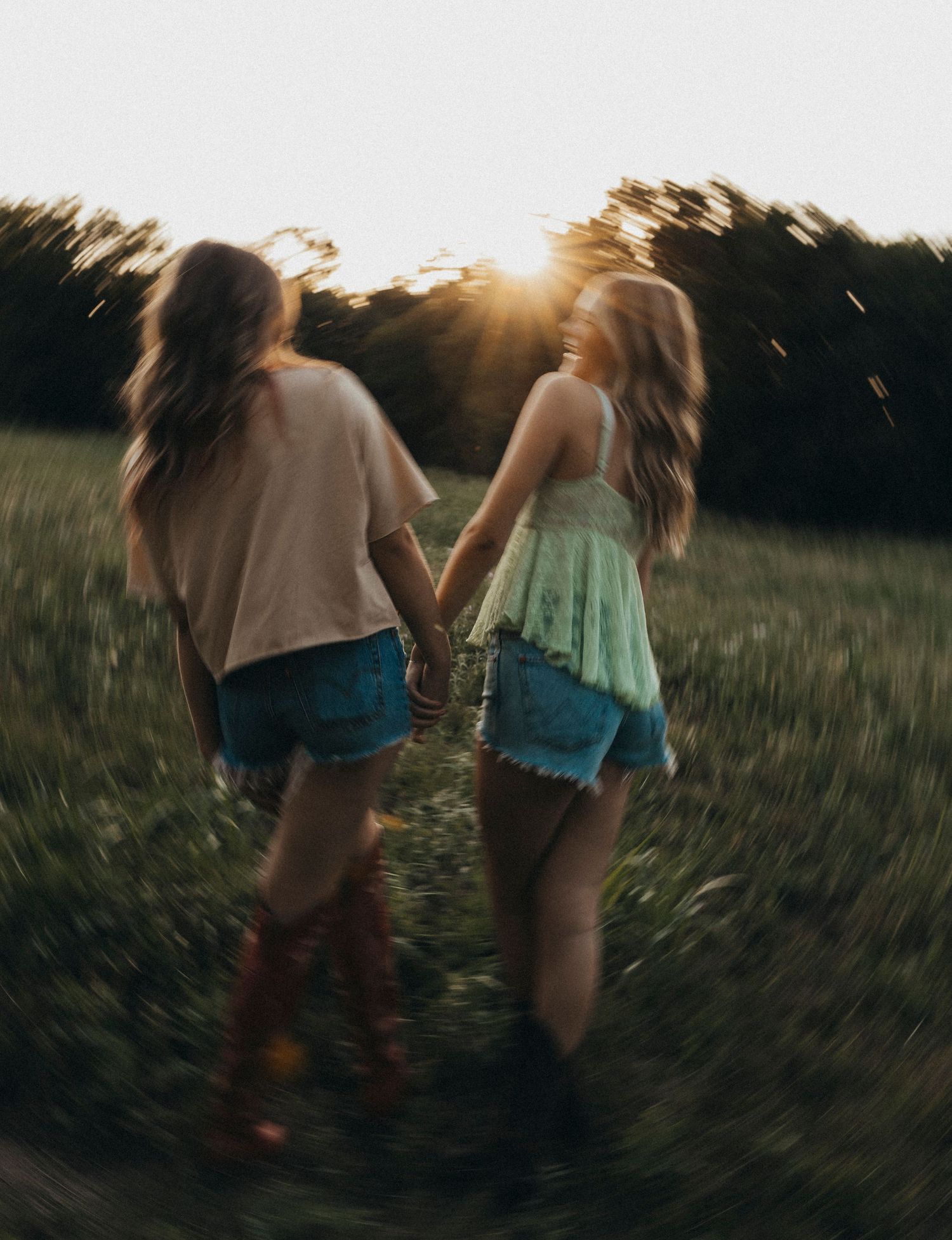 Two best friends walk hand in hand through a field at sunset during an outdoor summer photoshoot in Abilene, Texas