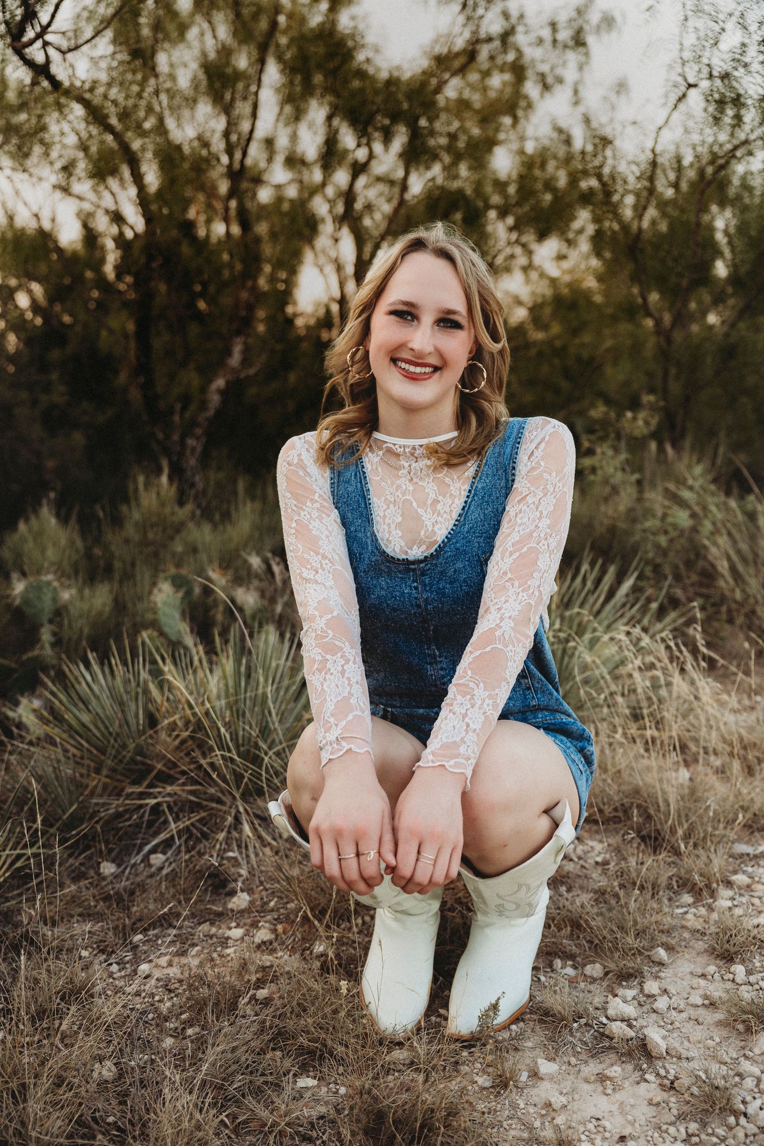 Smiling high school senior seated among native Texas grasses during a natural light senior portrait session in Abilene, Texas.
