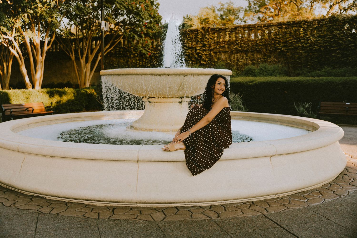 Cooper High School senior sitting on the edge of a fountain in downtown Abilene, TX during a warm golden hour senior session.
