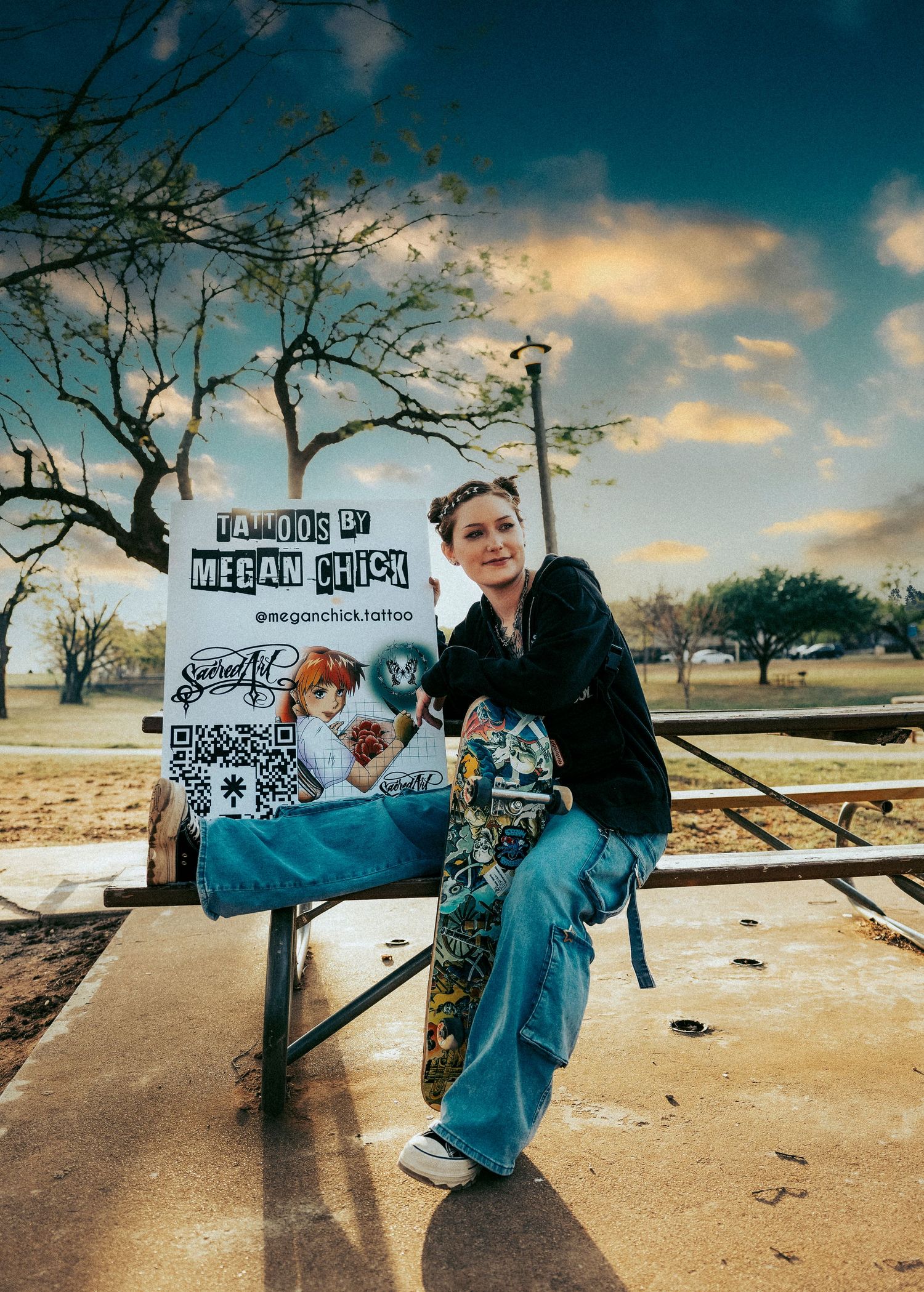 Woman posing with a Tattoos by Megan Chick promotional sign outdoors in a park setting.