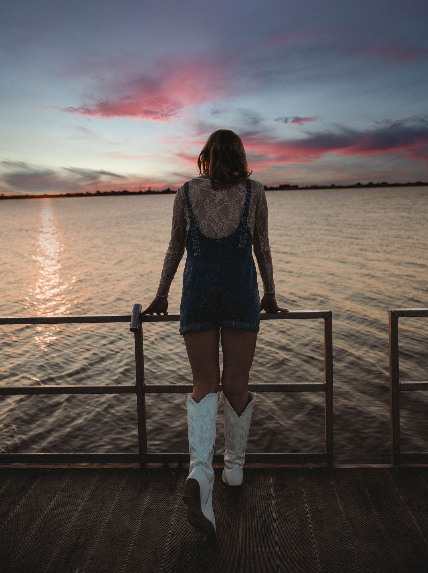 High school senior overlooking the lake from a dock at sunset during a golden hour senior portrait session in Abilene, Texas.