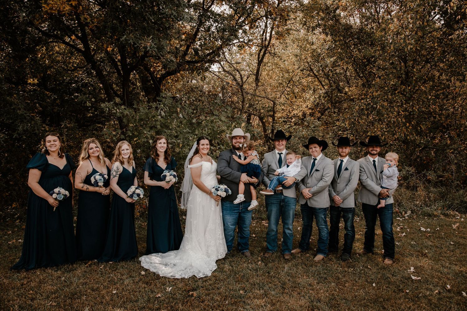 Wedding party in navy and gray attire poses together in autumn outdoor setting.