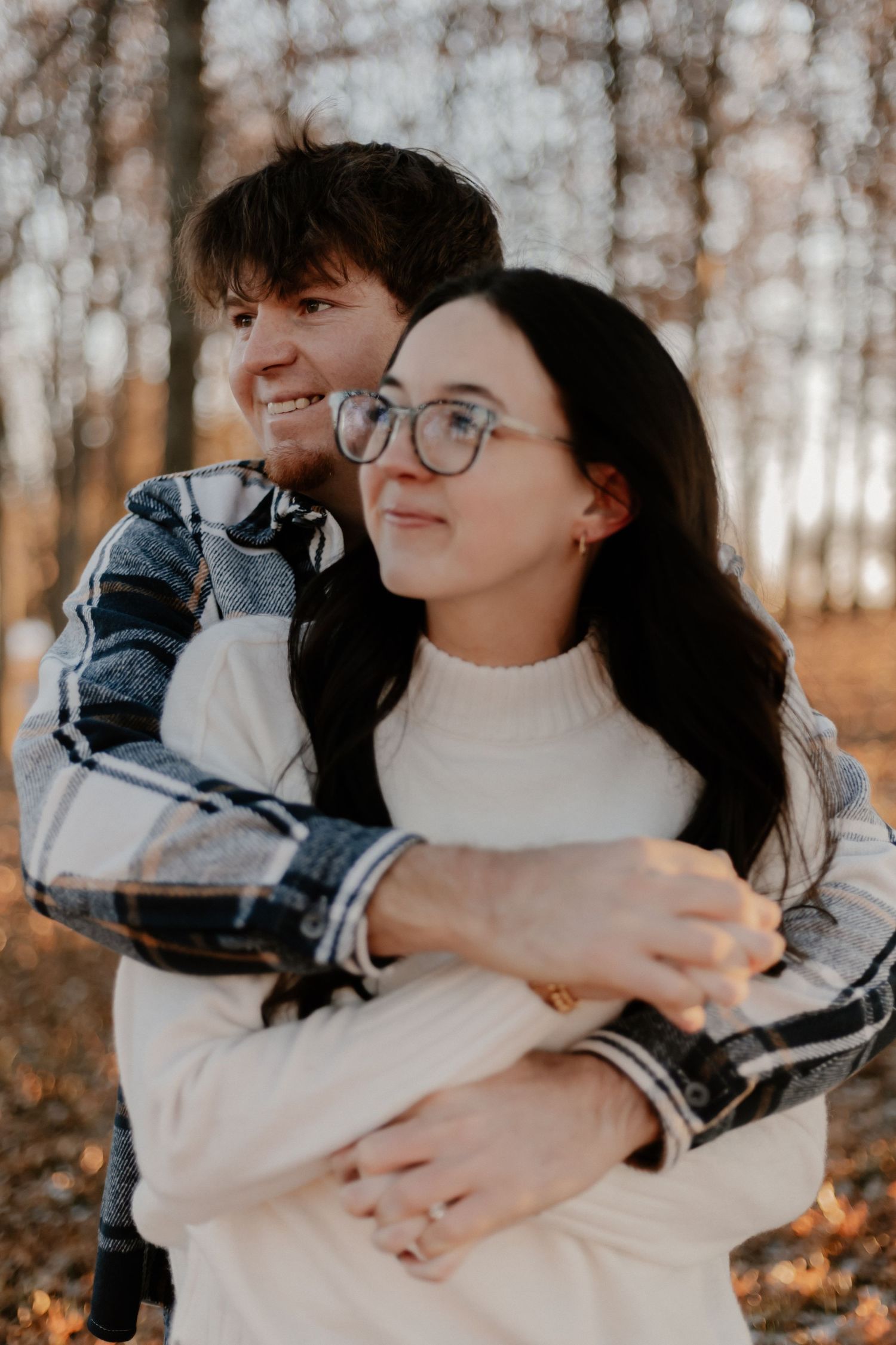 Couple embracing in a wooded area during autumn wearing cozy sweaters.